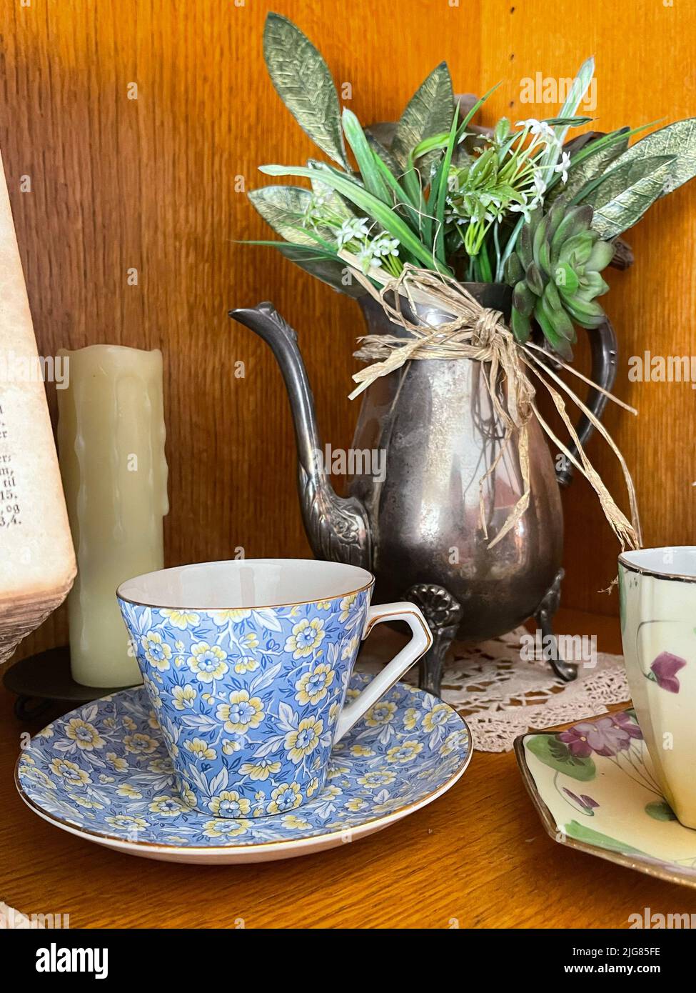 Una foto verticale di un'antica tazza di caffè in porcellana floreale con una teiera in metallo d'epoca sullo sfondo Foto Stock