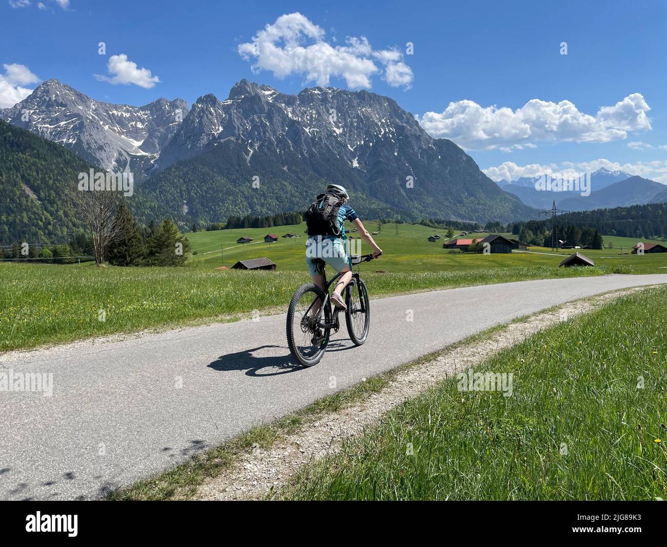 Donna in bicicletta, vista sui prati di caccia e fienile a Karwendel montagne, donna, natura, montagne, cielo blu, Attività, Tonihof, Alpenwelt Karwendel, Mittenwald, alta Baviera, Germania Foto Stock