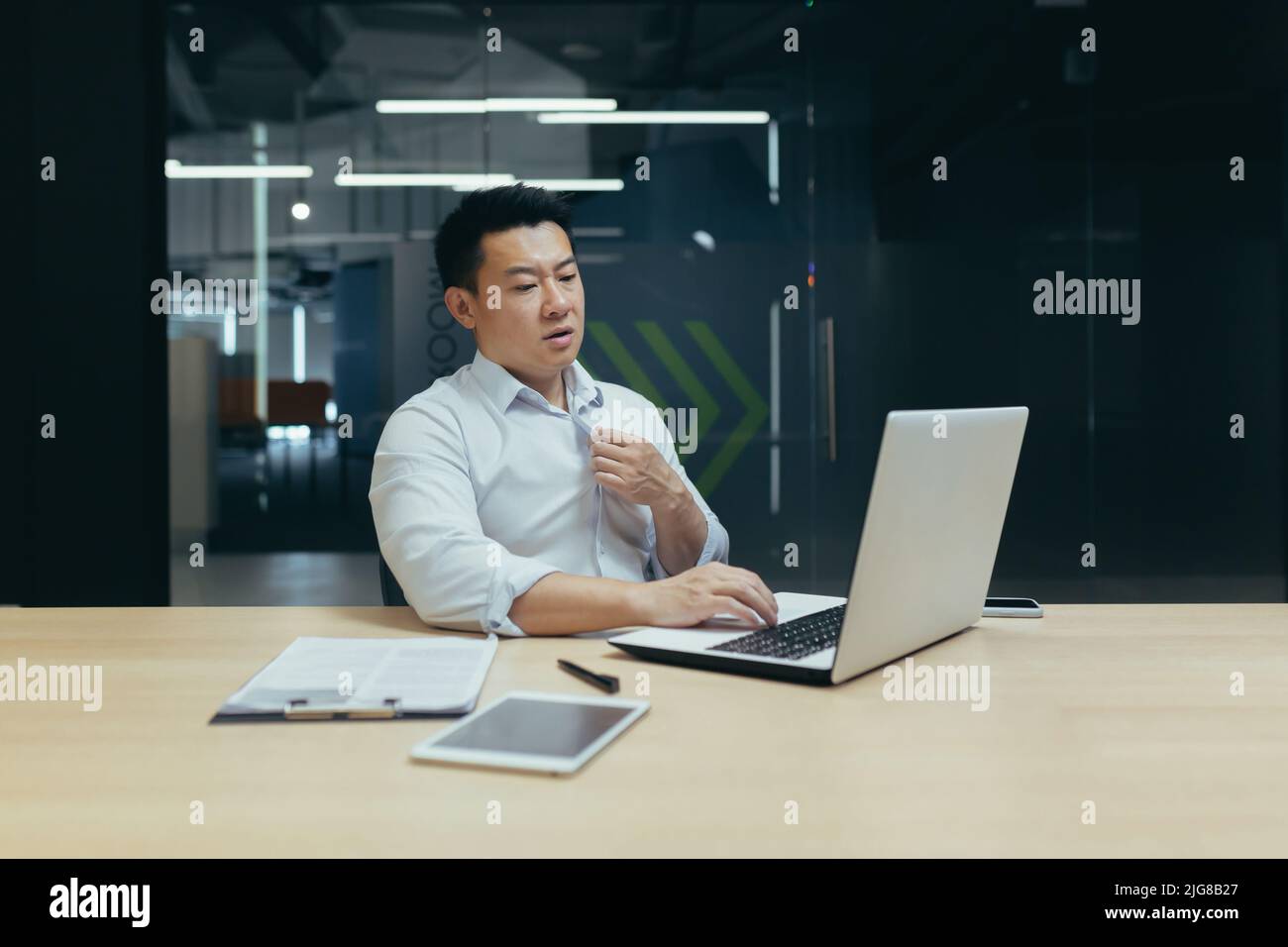 Il calore e la mancanza di aria in ufficio, un uomo asiatico lavora su un computer portatile, è caldo e non c'è aria condizionata. Foto Stock
