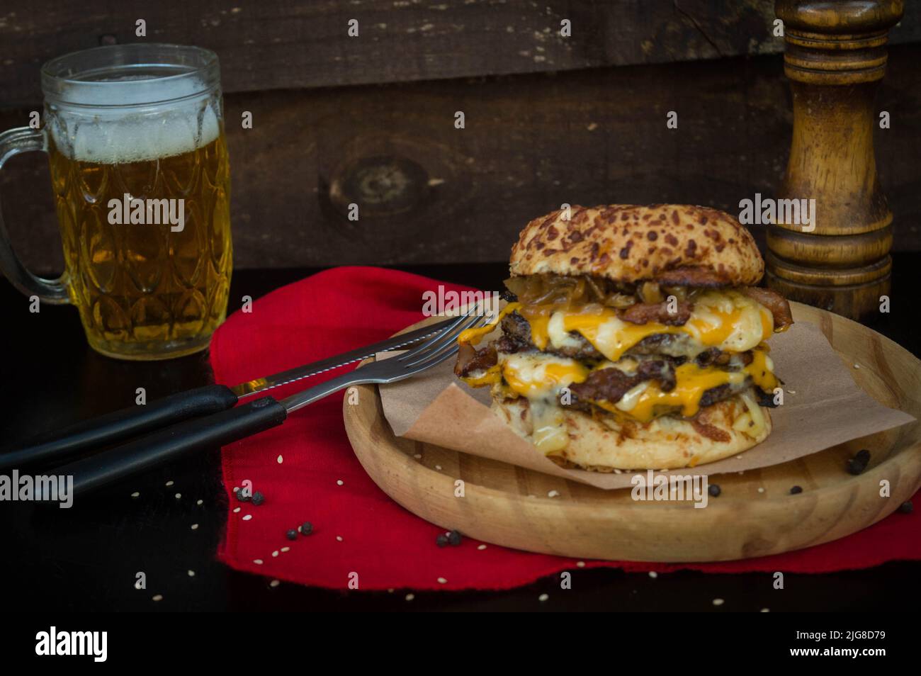 Un primo piano di hamburger su tavola circolare di legno vicino a un bicchiere di birra Foto Stock