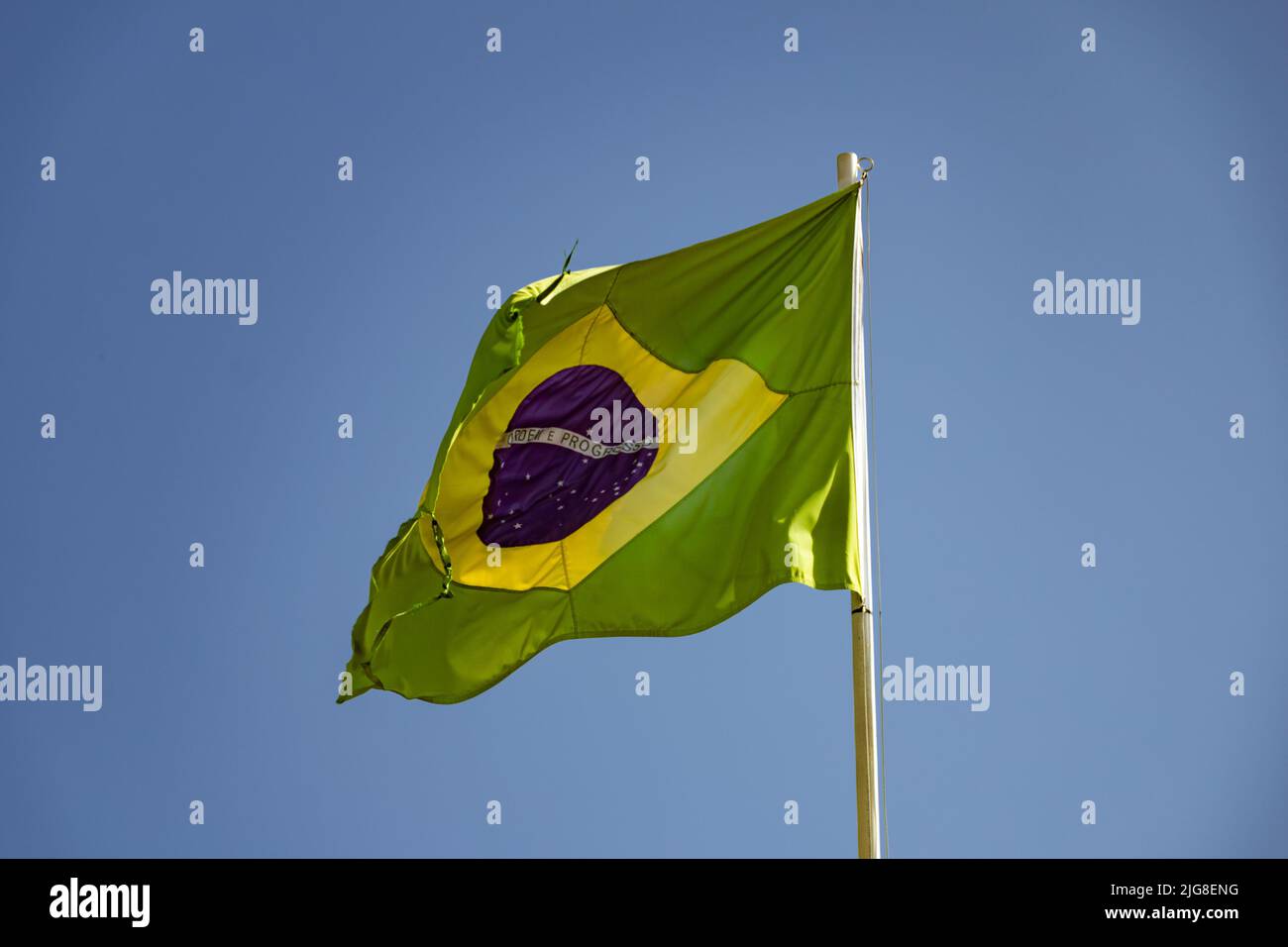 Goiania, Goiás, Brasile – 08 luglio 2022: Una vecchia bandiera brasiliana, strappata e sfilacciata, sventolando nel vento. Foto Stock