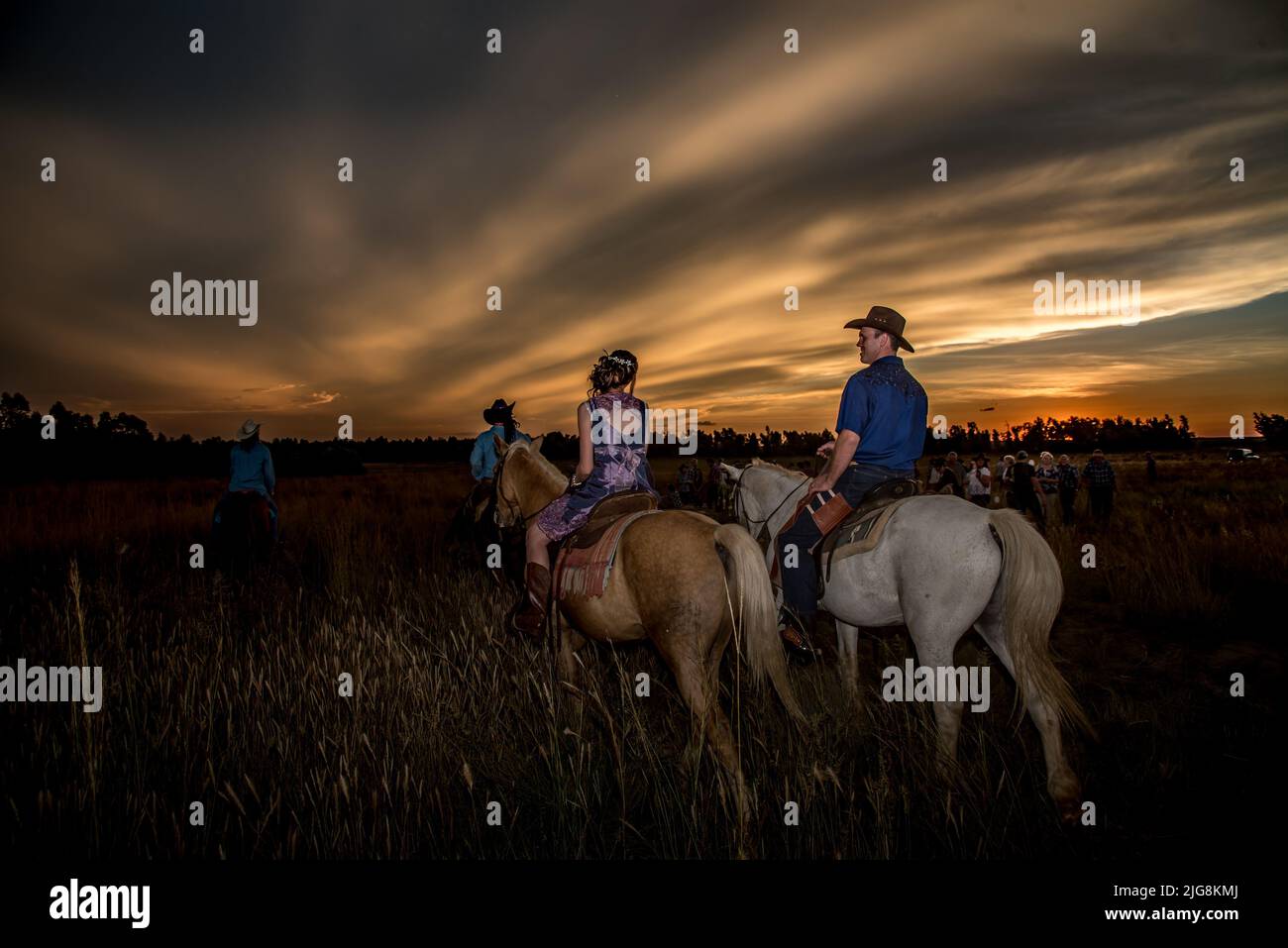 Una vista posteriore di una coppia di cavalli che cavalcano al tramonto dopo essersi sposati Foto Stock