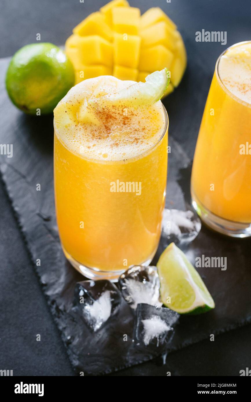 Succo di mango su sfondo scuro. Drink estivo con ghiaccio e fettine di mango e lime. Foto Stock