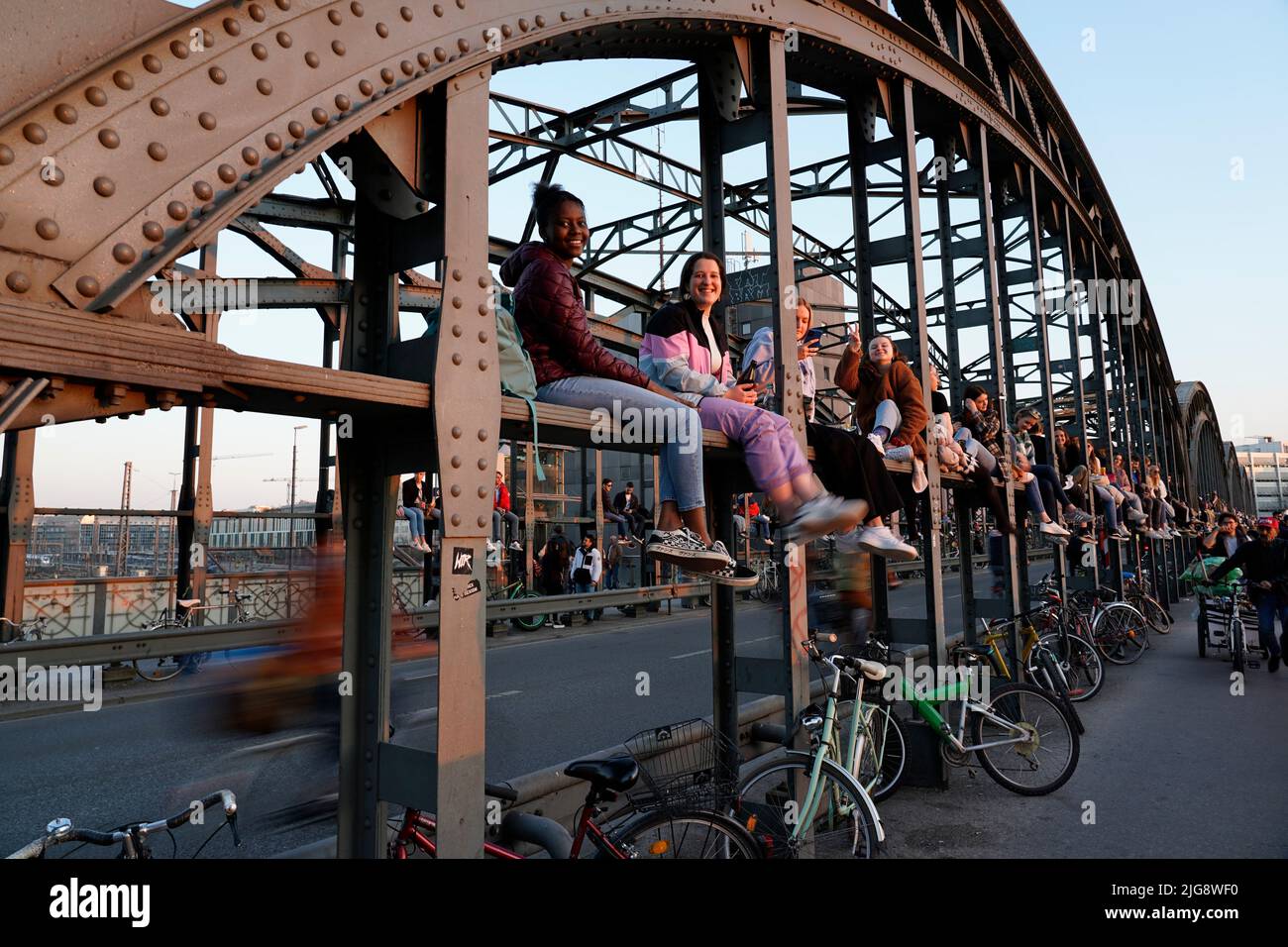 Germania, Baviera, Monaco, Haccurbrücke, giovani si siedono sulla costruzione del ponte e godersi il tramonto Foto Stock