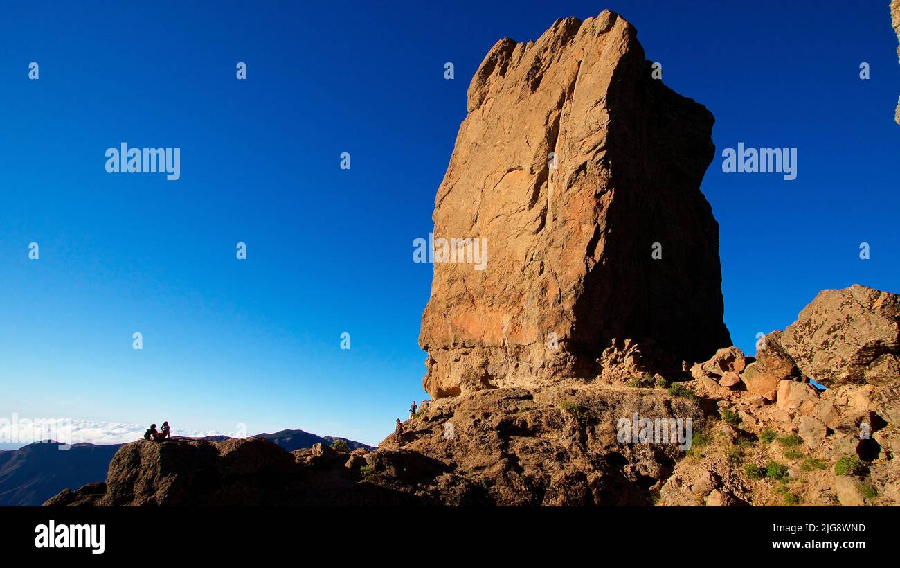 Spagna, Isole Canarie, Gran Canaria, Massif Central, Roque Nublo, scatto grandangolare, blu cielo acciaio, roccia monolitica, luce da sera, coppia seduta da dietro Foto Stock