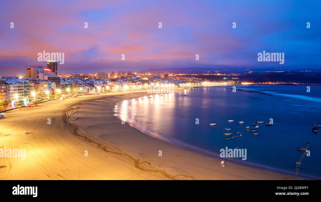 Spagna, Isole Canarie, Gran Canaria, Las Palmas, Playa de las Canteras, alba, nuvole rosa, azzurro cielo, riflesso di luci sul mare, spiaggia sabbiosa, passeggiata illuminata, edifici a più piani, barche in acqua Foto Stock