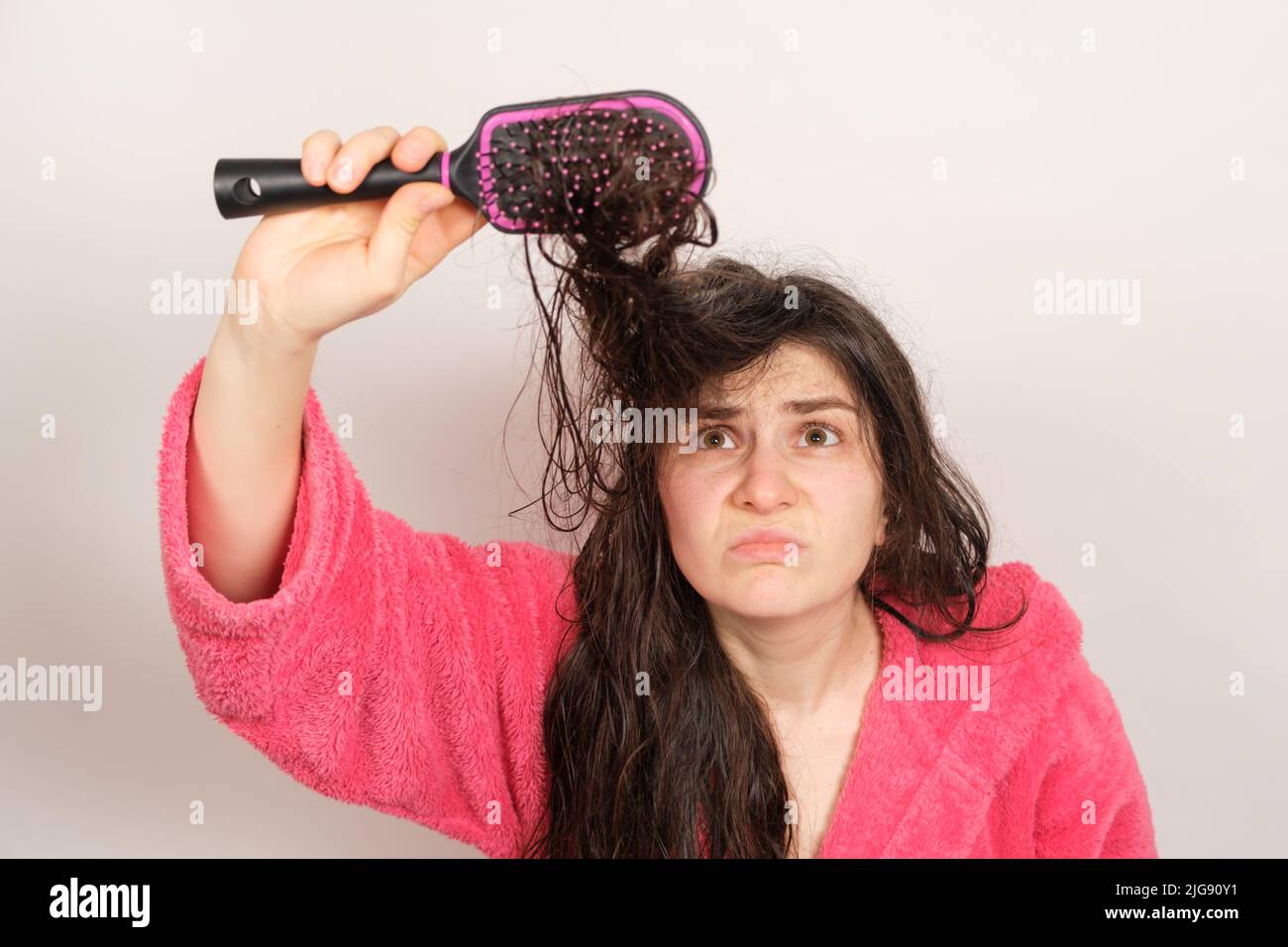 Una donna cerca di pettinare i capelli bagnati aggrovigliati. Cura dei capelli a casa, perdita dei capelli e sezione. Foto Stock