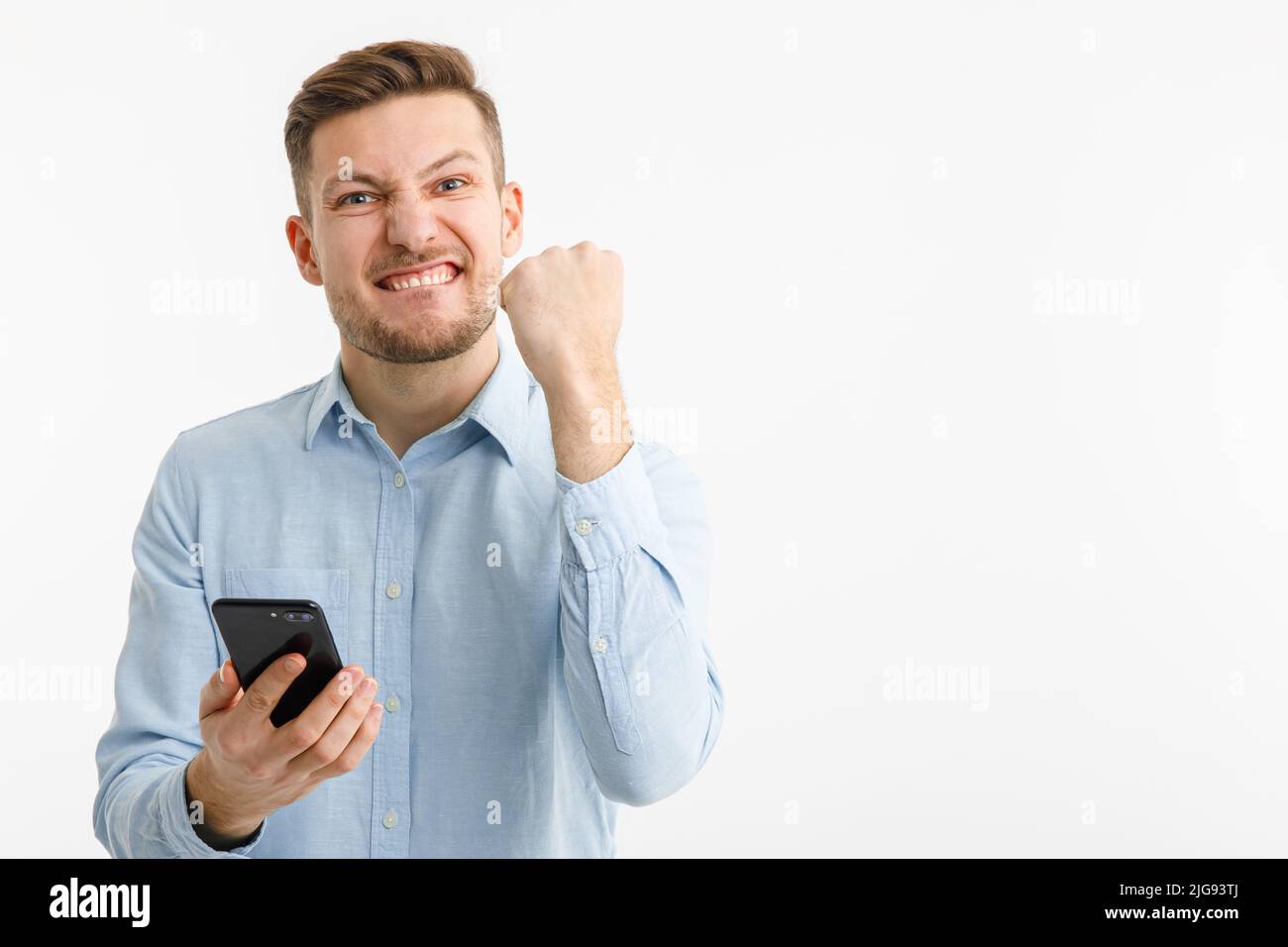 Un uomo tiene uno smartphone in mano e si rallegra di una transazione di successo sugli scambi cripto. Isolato su sfondo bianco. Foto Stock