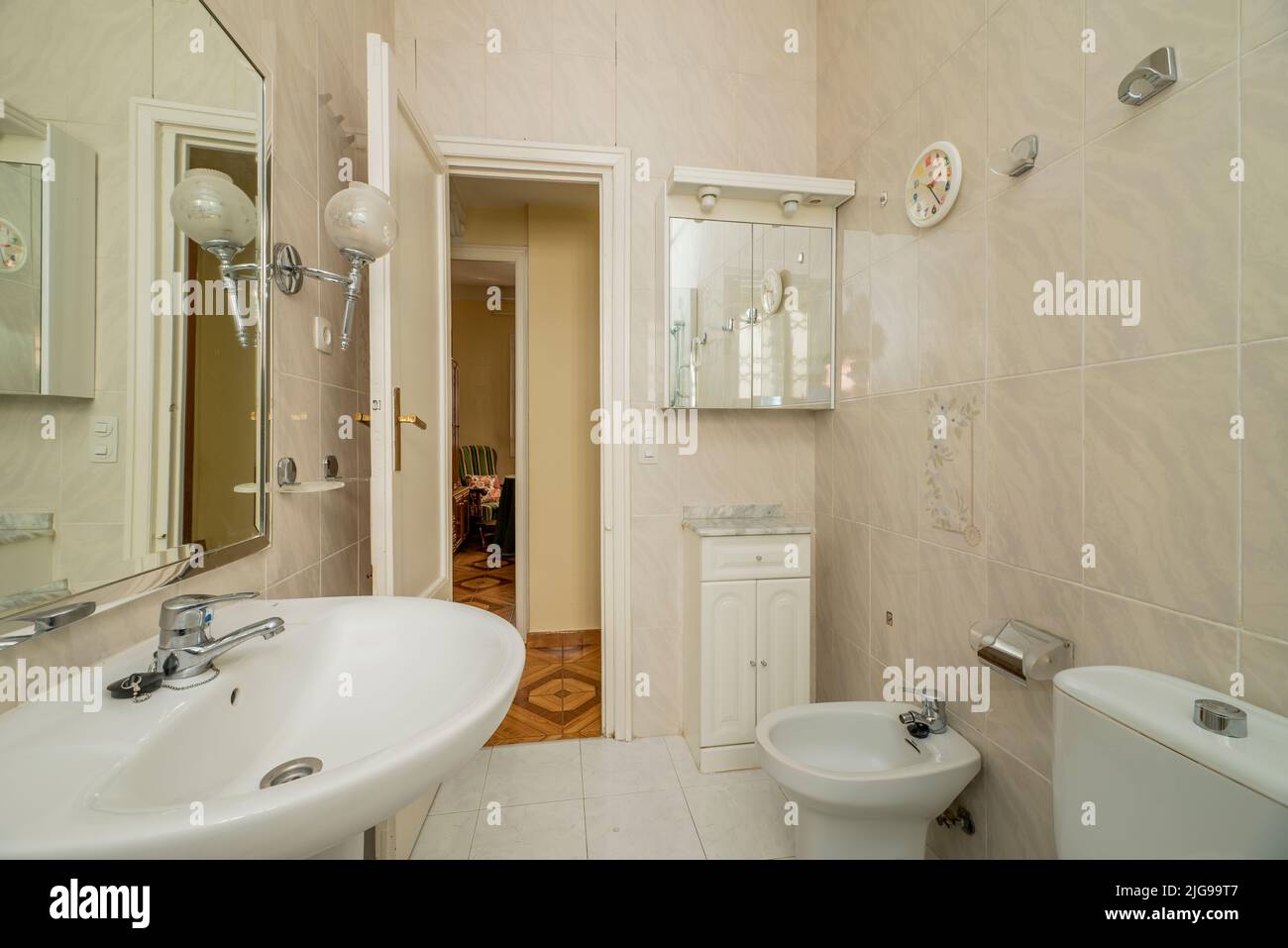 Bagno con mobili in legno bianco, specchio incorniciato e WC in porcellana bianca Foto Stock