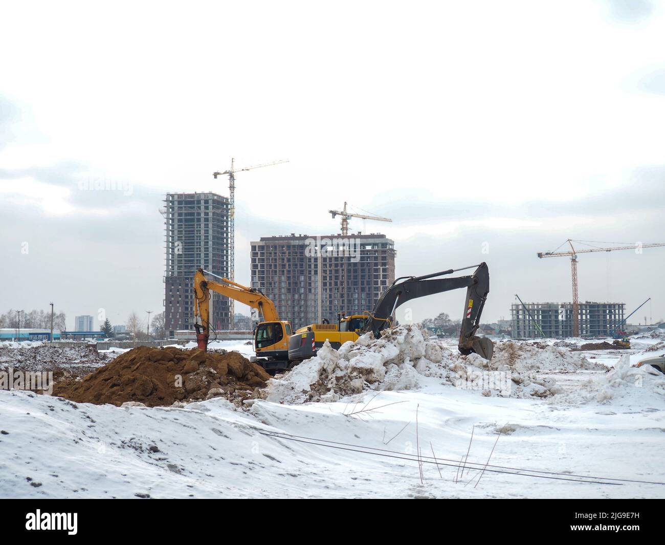 Costruzione di alti edifici in inverno. Il lavoro degli escavatori. Opere di terra. Pozzi di scavo. Strutture per costruzioni in calcestruzzo. Montagne della terra Foto Stock