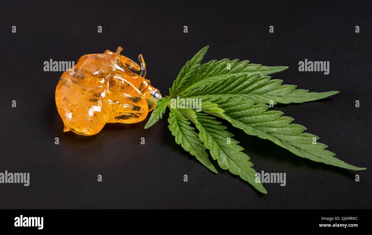 alto thc, pezzi di cera di cannabis giallo dorato e foglia verde, la marijuana si concentrano sul retro scuro. Foto Stock