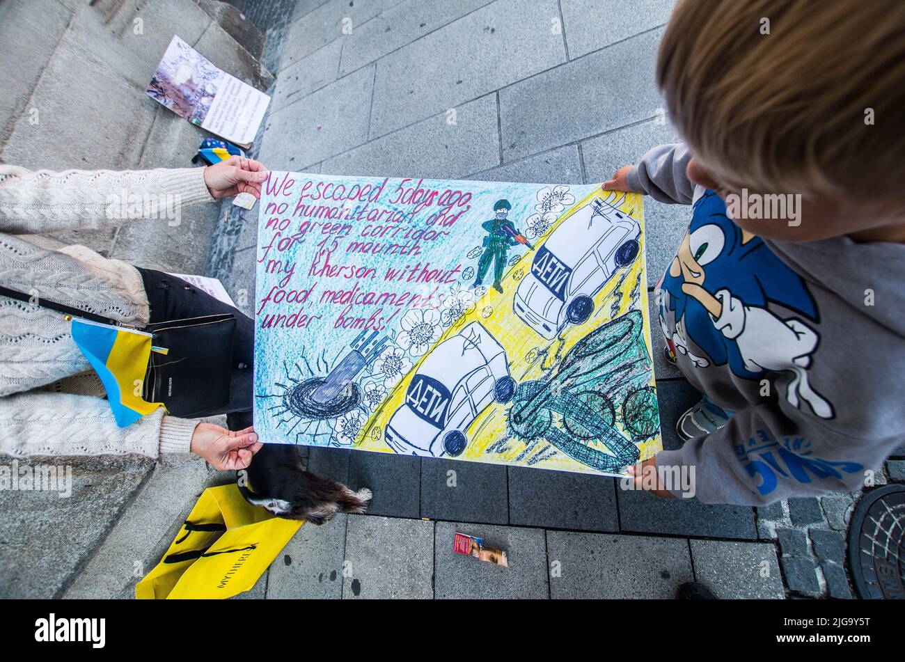 Monaco, Baviera, Germania. 8 luglio 2022, Monaco di Baviera, Germania: Un rifugiato ucraino di cinque anni a Monaco di Baviera, Germania, si accoccolò contro un muro per provocare pensiero nei passanti, mentre sua madre poi spiega come sono fuggiti Kherson con il loro cane, nonostante parlino di loro, dichiarano che non c'erano corridoi umanitari. Ora, nel quinto mese della piena invasione dell'Ucraina, dei rifugiati ucraini e degli immigrati a Monaco, la Germania ha dimostrato l'azione decisiva del Politik tedesco nel sostenere la difesa territoriale dell'Ucraina. Credit: ZUMA Press, Inc./Alamy Live News Foto Stock