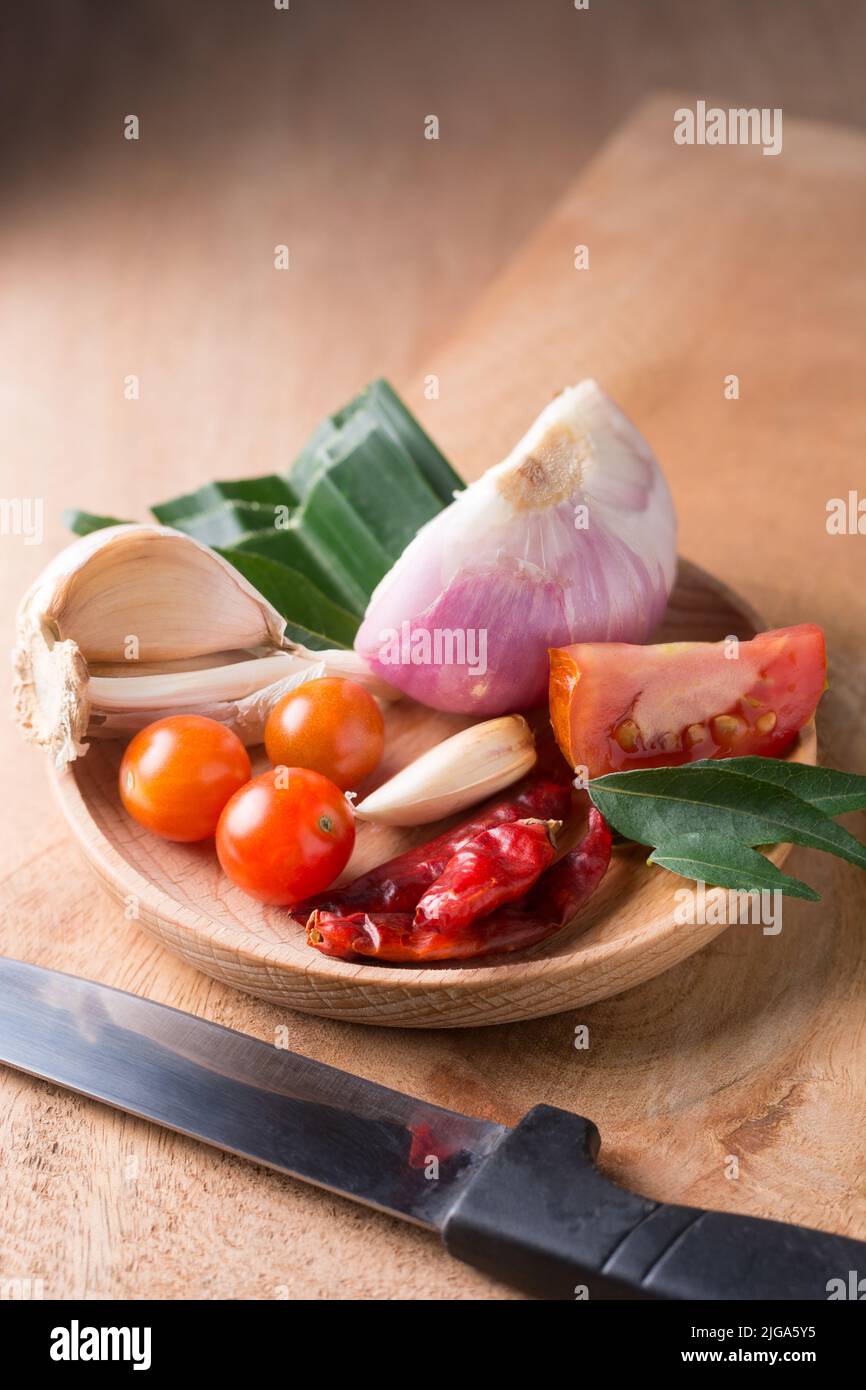 verdure, ingredienti aromatizzanti comuni per la cucina asiatica e sud-asiatica, erbe e spezie per cucinare su un piatto di legno con un coltello Foto Stock