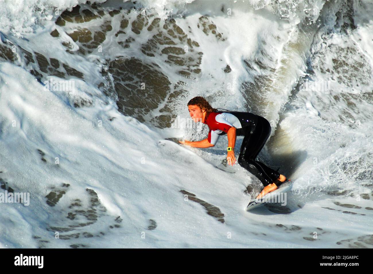 Un giovane uomo adulto californiano surfer cattura l'onda perfetta mentre taglia attraverso l'acqua sulla sua tavola da surf nell'oceano. Foto Stock