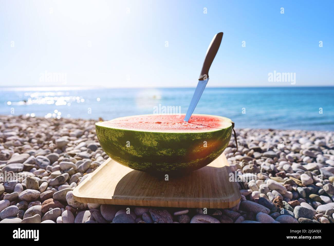 Mezzo anguria sulla spiaggia con ciottoli all'alba. Vacanza in mare con un pic-nic sulla riva. Foto Stock