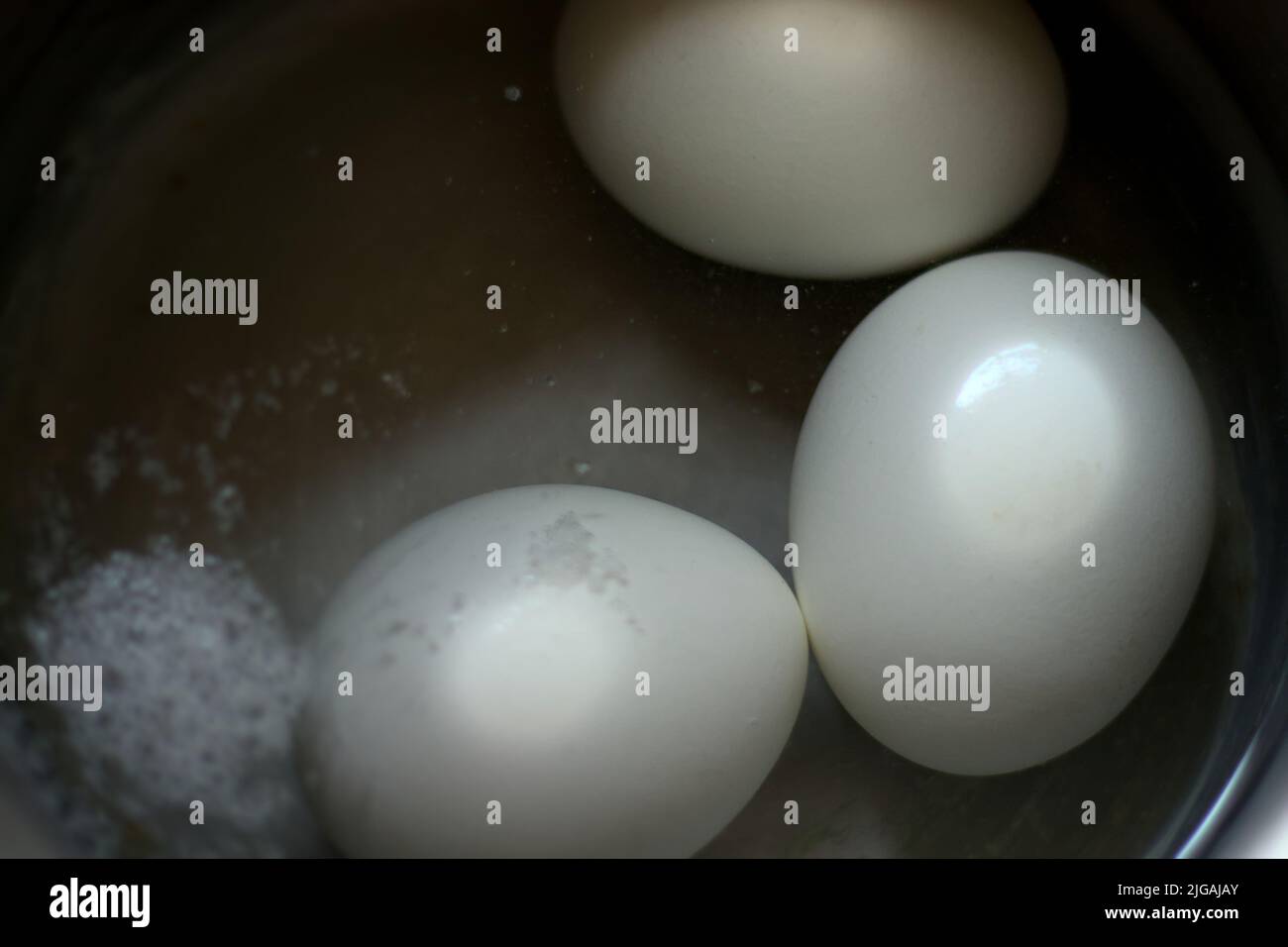 tre uova bollite in una pentola di acciaio inossidabile riempita di acqua calda Foto Stock