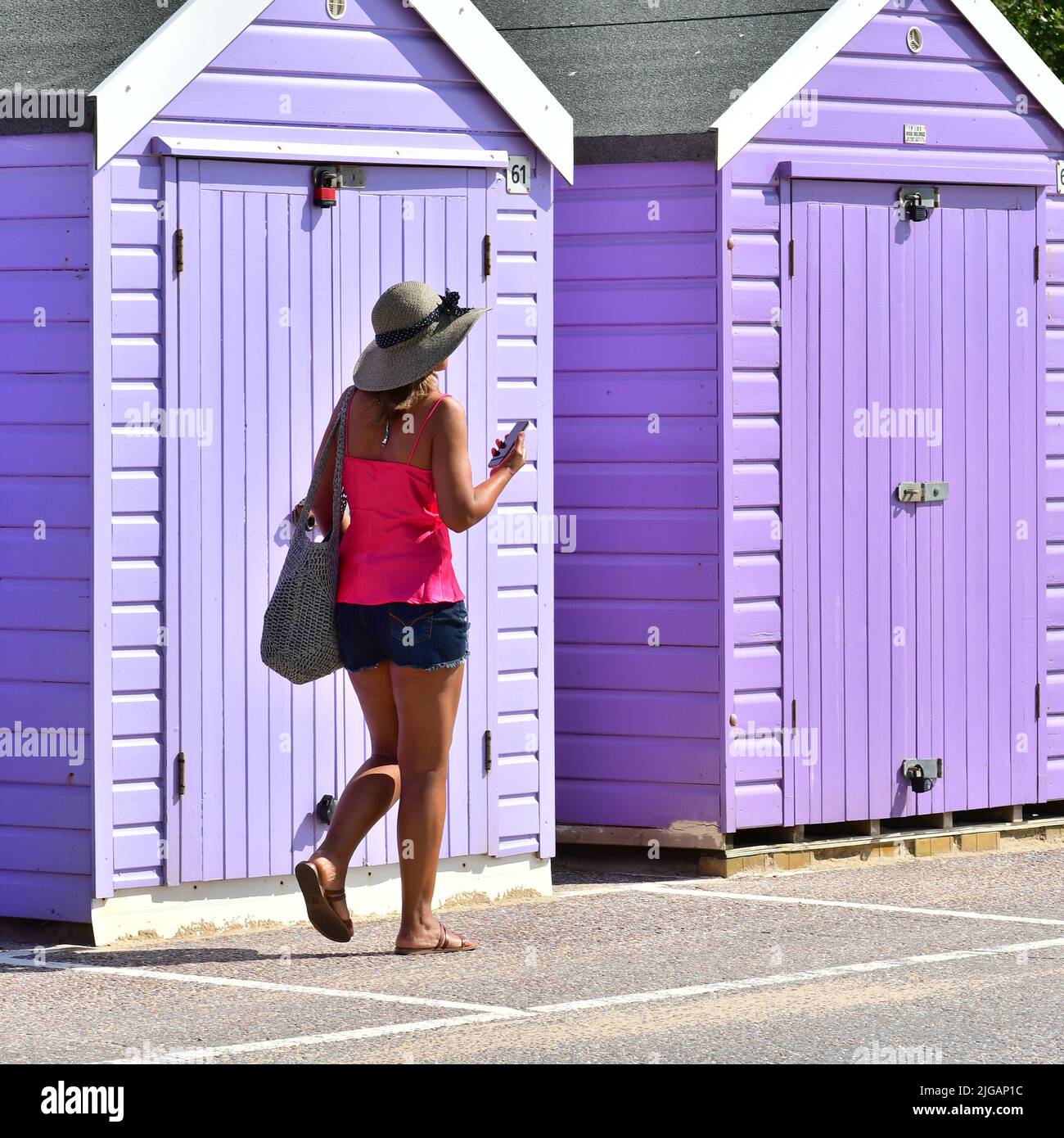Bournemouth, Dorset, Inghilterra, Regno Unito, 9th luglio 2022, Meteo. Onda termica. La gente in spiaggia la mattina. Donna in un cappello e top rosa passeggiando oltre capanne viola spiaggia. Credit: Paul Biggins/Alamy Live News Foto Stock