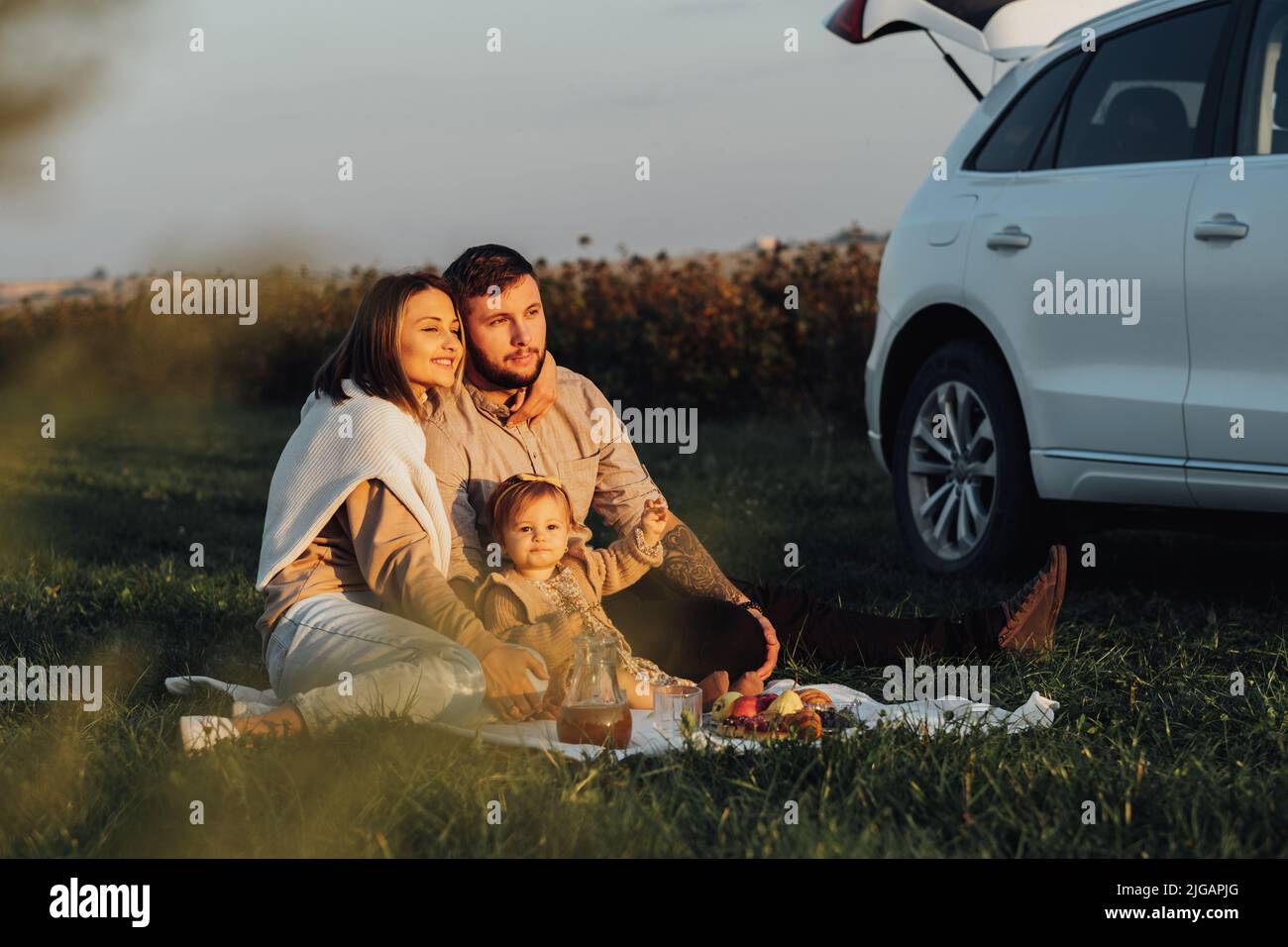 Happy Young Family Goding Road Trip su SUV Car, mamma papà e la loro figlia del bambino che hanno picnic nel weekend all'aperto al tramonto Foto Stock