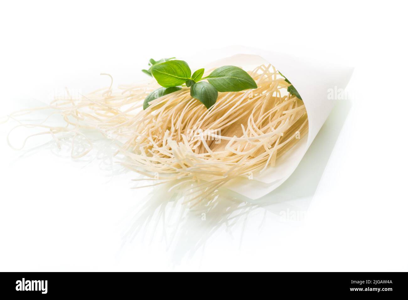 spaghetti fatti in casa secchi in sacchetto di carta con basilico, isolato su sfondo bianco Foto Stock