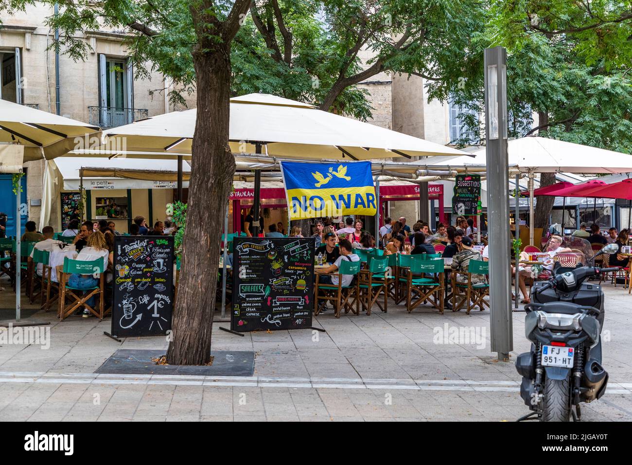 Una bandiera ucraina con la scritta "Niente Guerra" è appesa tra gli ombrelloni di un caffè di strada a Montpellier, in Francia, sopra tavoli affollati. Tali striscioni sono apparsi in molte città europee nel 2022 come segno di solidarietà dopo l'invasione russa dell'Ucraina. Foto Stock