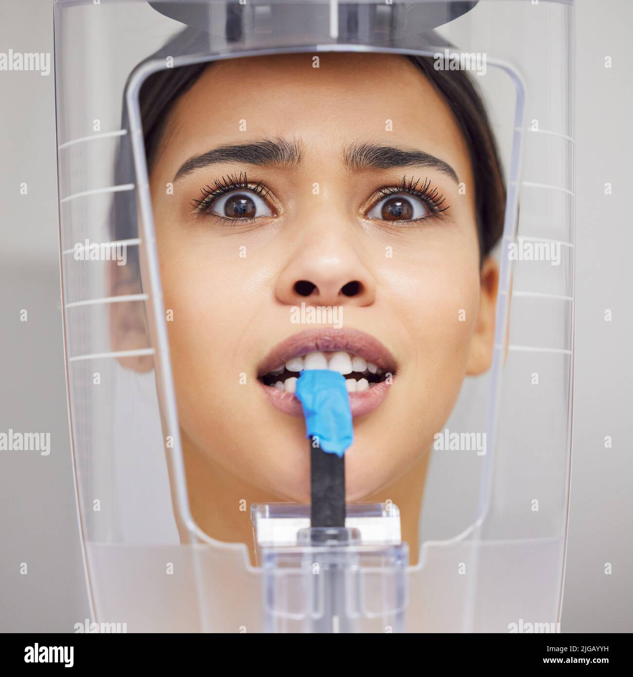 Quanto tempo devo rimanere così: Una giovane donna che guarda ansiosa mentre usa una macchina a raggi X in un ufficio dentistico. Foto Stock