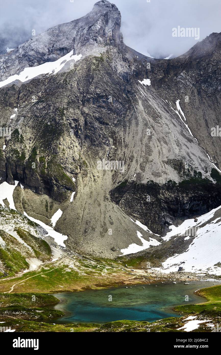 Un colpo verticale di un piccolo lago ai piedi delle alte Alpi ricoperte di nuvole Foto Stock Un colpo verticale di un piccolo lago ai piedi delle alte Alpi ricoperte di nuvole Foto Stock