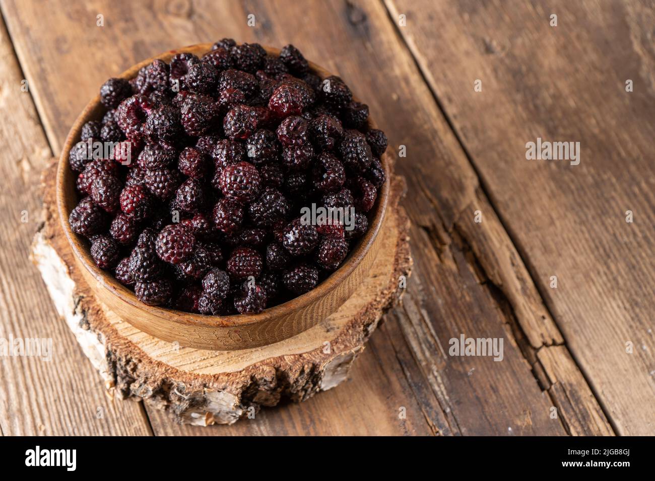 La bacca nera è un ibrido di lamponi e more. Bacche in una ciotola di legno sul tavolo. Vitamina estate cibo. Raccolto. Raspberry e blackberry. Lampone nero. Foto Stock