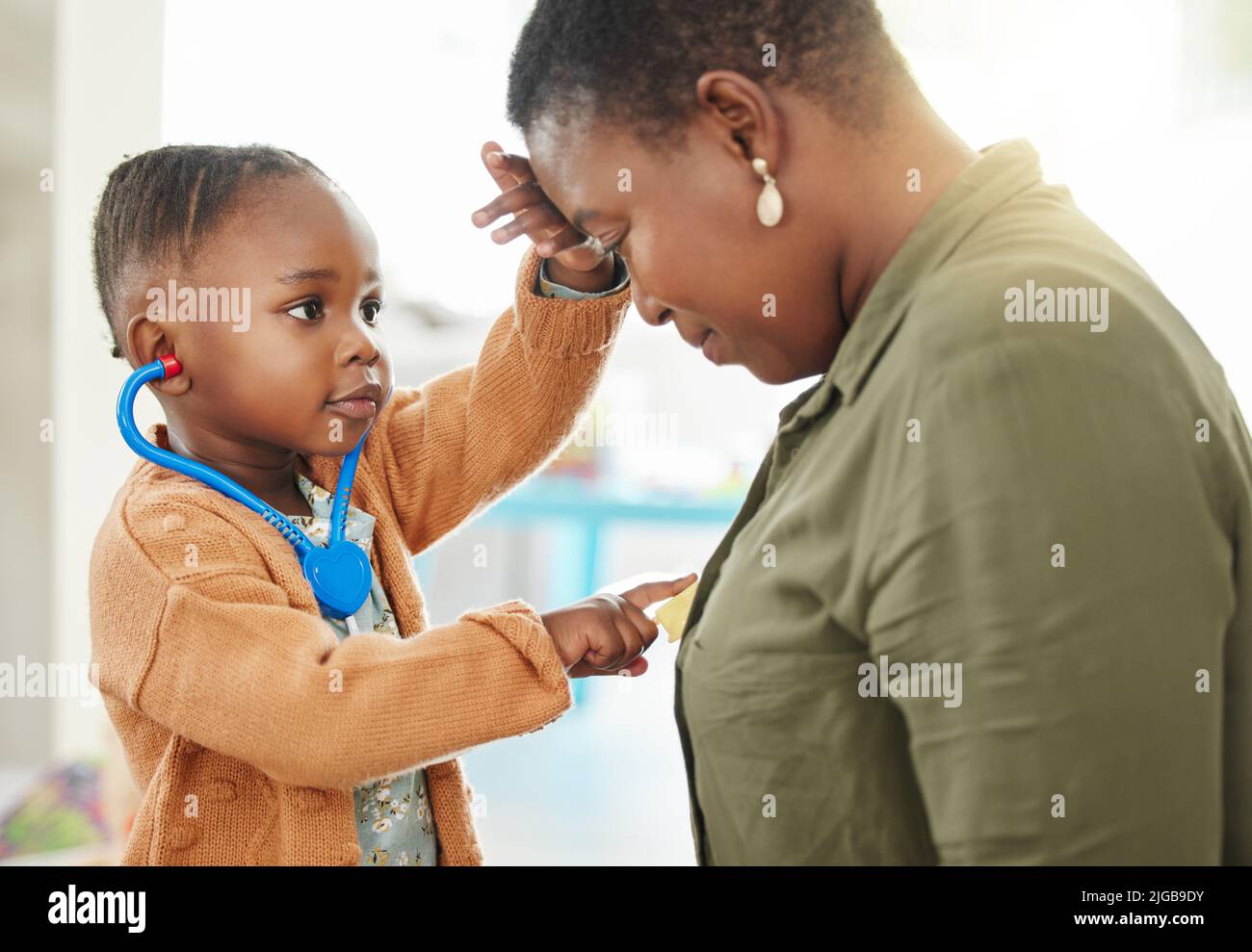 La testa sente mamma calda. Una bambina che gioca medico mentre ascolta il petto delle madri. Foto Stock