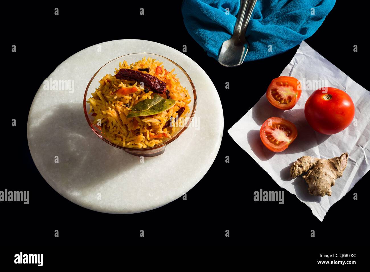 Il riso piccante al pomodoro o il pilaf o il pulav del Tamatar, è un piatto vegetariano dell'India del sud con foglie di curry, il peperoncino. Ciotola di vetro su sfondo nero. Vista dall'alto, primo piano. Foto Stock