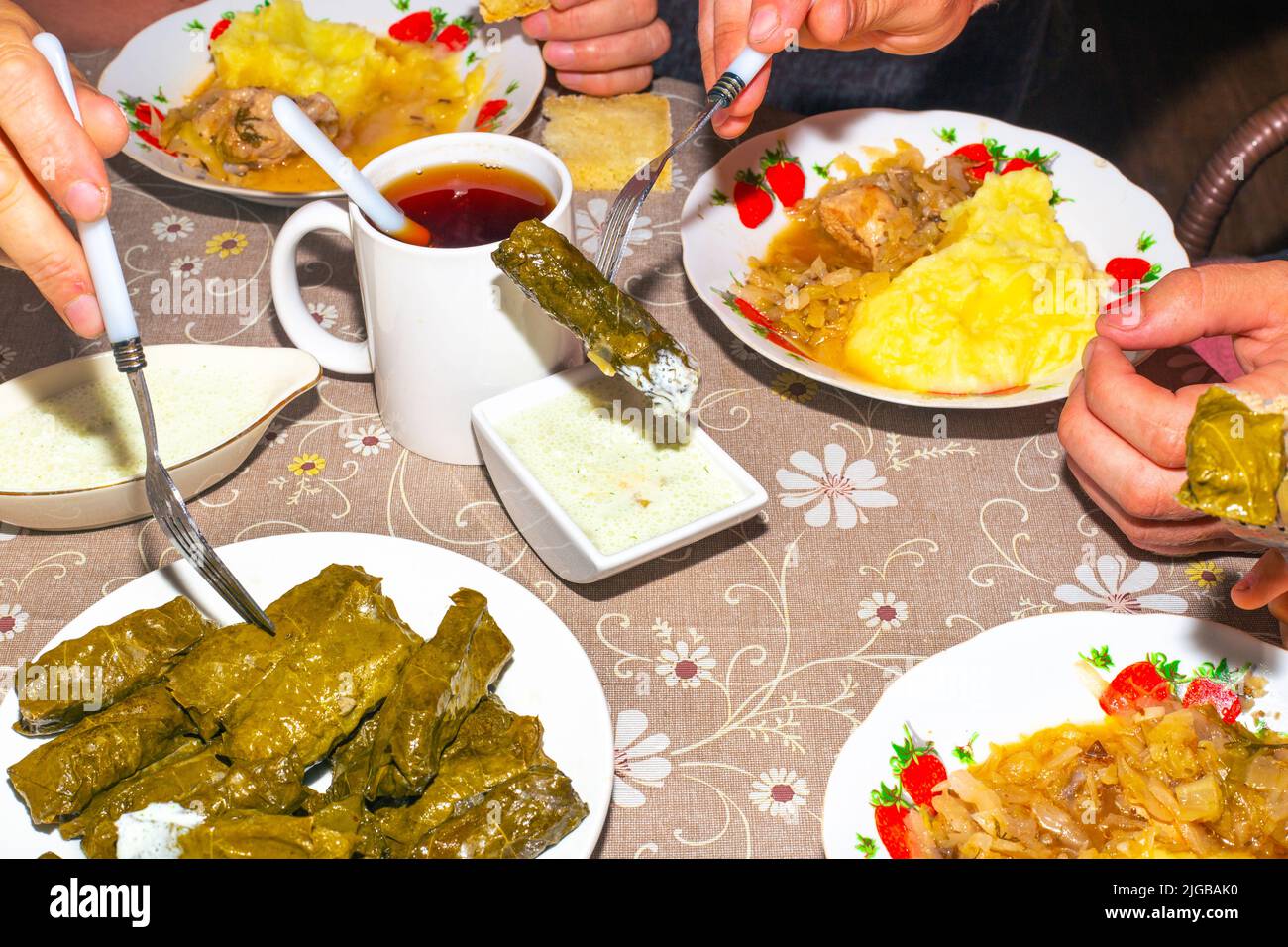 La famiglia sta mangiando al tavolo della cena. Dolma su un piatto, salsa e purè di patate con cavolo, tazze con bevande, vista dall'alto. Foto Stock