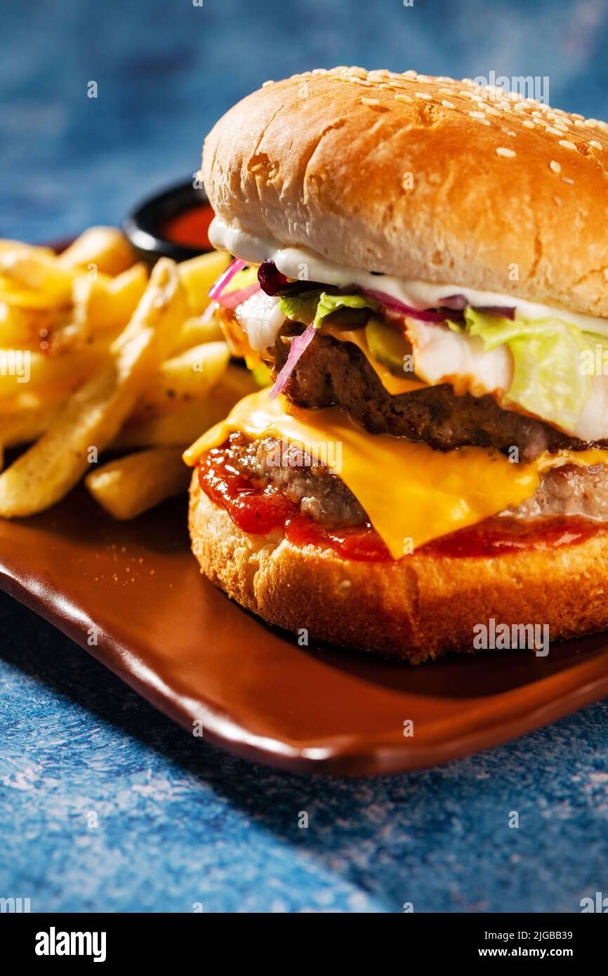 Hamburger. Succulenti cotolette di maiale, formaggio cheddar, cipolle croccanti sottaceto, lattuga avvolta in un panino sotto due salse. Servito con patatine fritte e salsa alla panna. Foto Stock