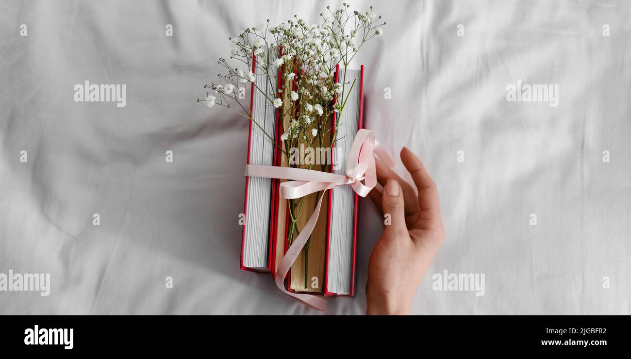 Mano femminile e libri legati con nastro e fiori sul letto Foto Stock