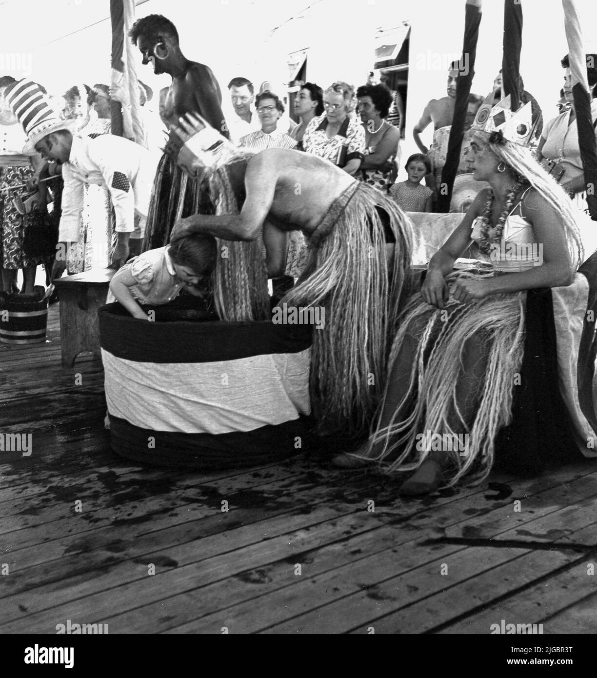 1950 anni, un bambino piccolo e storico che sta per farsi immergere la testa in acqua come parte di una cerimonia di "attraversamento dell'equatore" Re Nettuno a bordo di una nave da crociera Union-Castle. Foto Stock