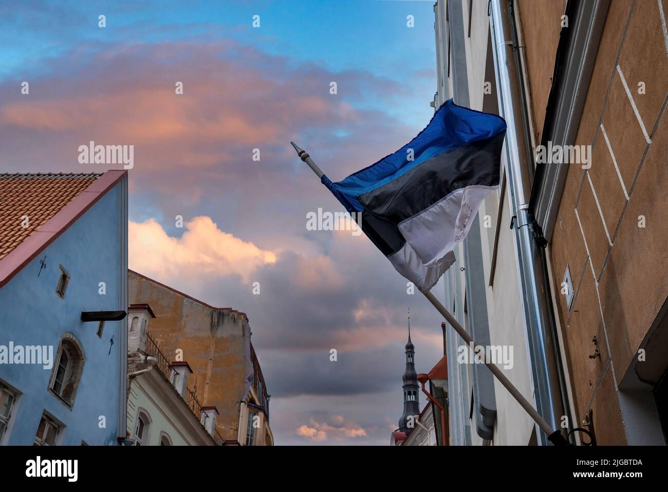 Vista ad angolo basso della bandiera estone che sventola contro gli edifici della città durante il tramonto Foto Stock