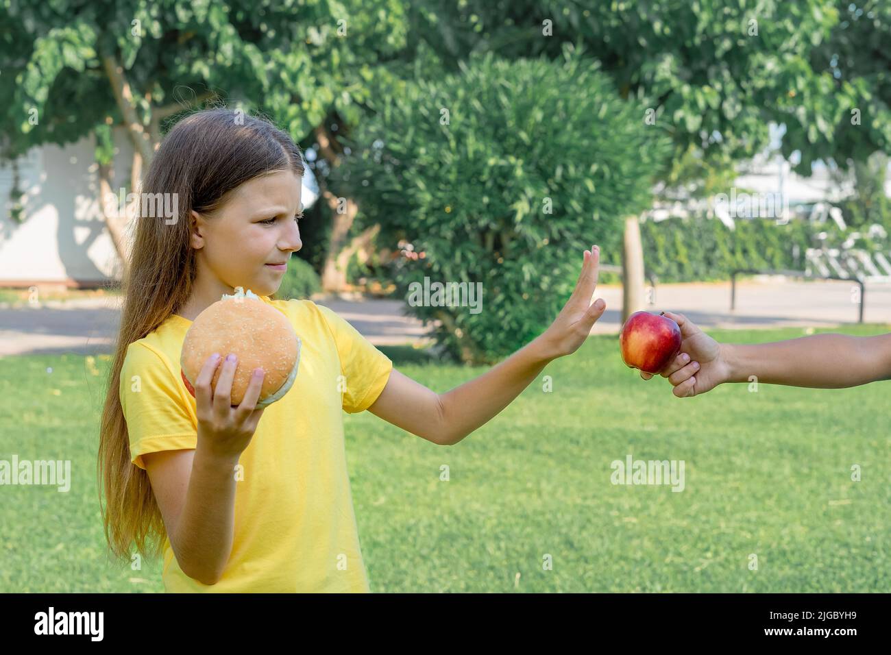 Una ragazza adolescente rifiuta una mela sana a favore di un hamburger. Cibo malsano. Foto Stock