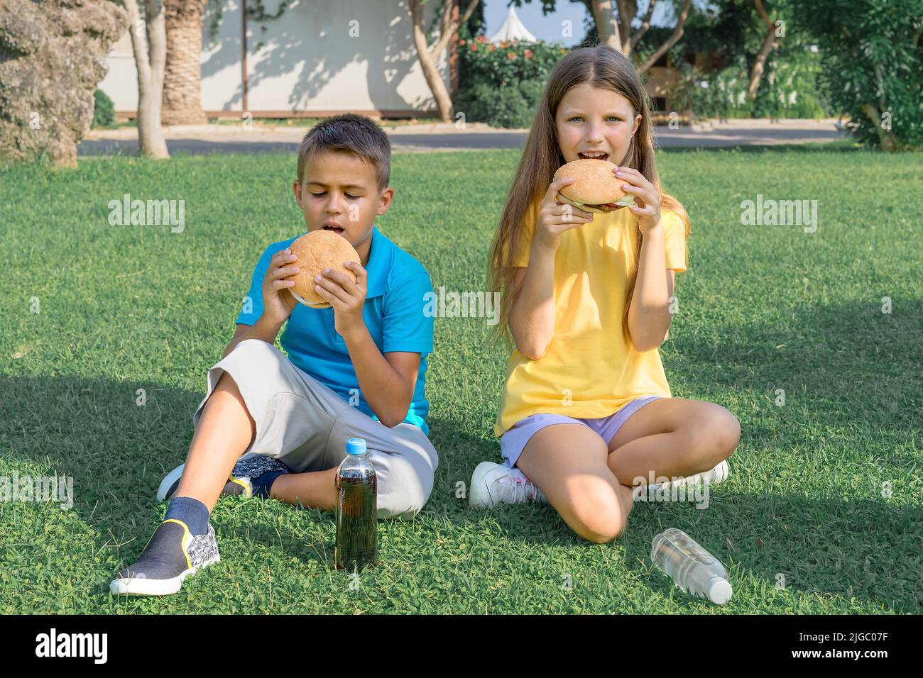 Bambini gli scolari mangiano gli hamburger nel parco seduti sull'erba. Pranzo scolastico. Foto Stock