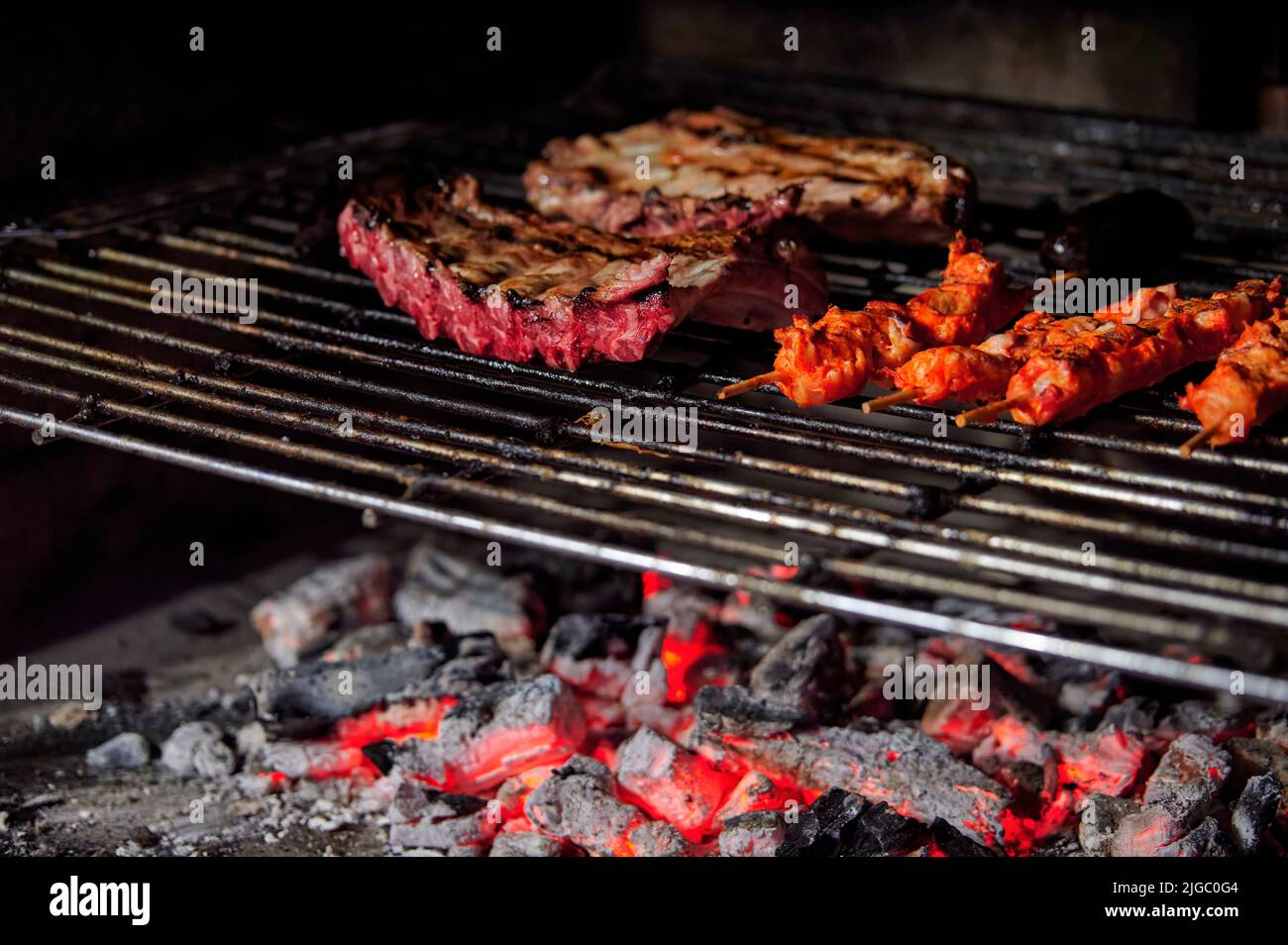 Costolette di maiale e spiedini di pollo marinati che cucinano su carbone su una griglia barbecue Foto Stock