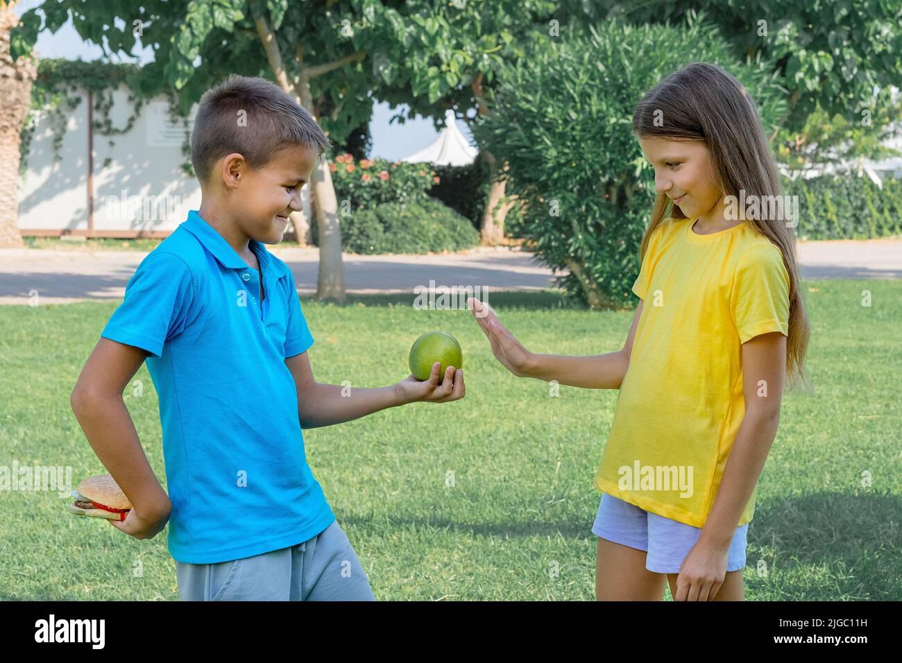 Ragazzo e ragazza adolescenti con mela e hamburger nel parco. Scelta tra cibo sano e malsano. Foto Stock