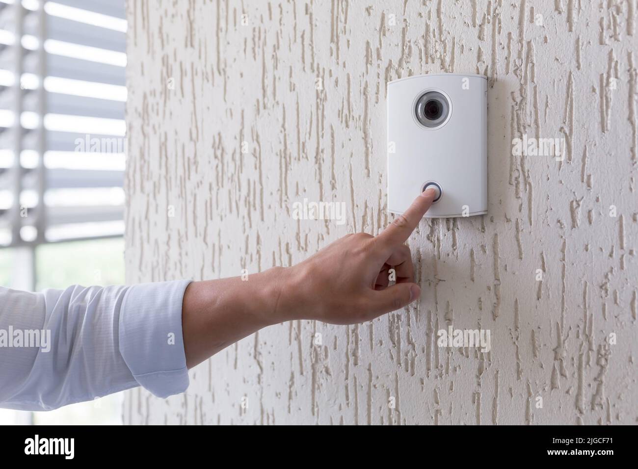 Mano di un uomo in una camicia bianca premendo il pulsante di una porta bussare su una parete bianca di una casa, un intelligente porta bussare con una videocamera per la comunicazione Foto Stock