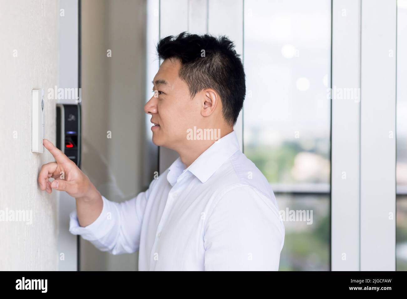 L'uomo asiatico usa un batticalcagno con una videocamera per aprire la porta. Foto Stock