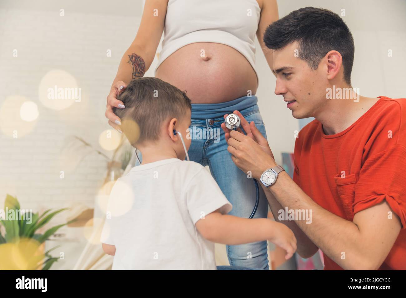 giovane uomo che aiuta suo figlio ad ascoltare il battito del cuore di un bambino nel ventre di sua moglie, famiglia felice. Foto di alta qualità Foto Stock