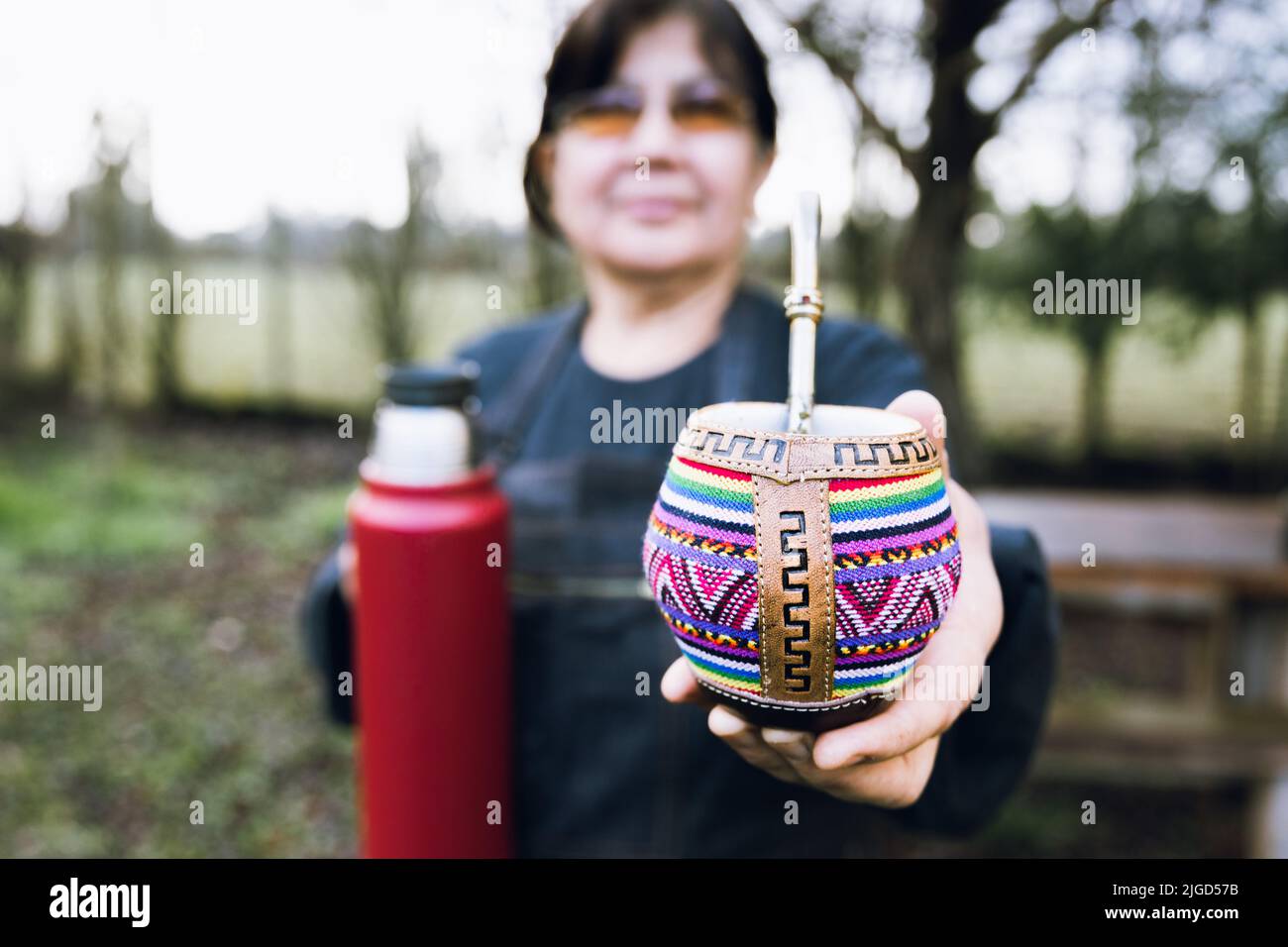 Donna latina che serve compagno con un termo rosso, in un colorato compagno etnico. Foto Stock