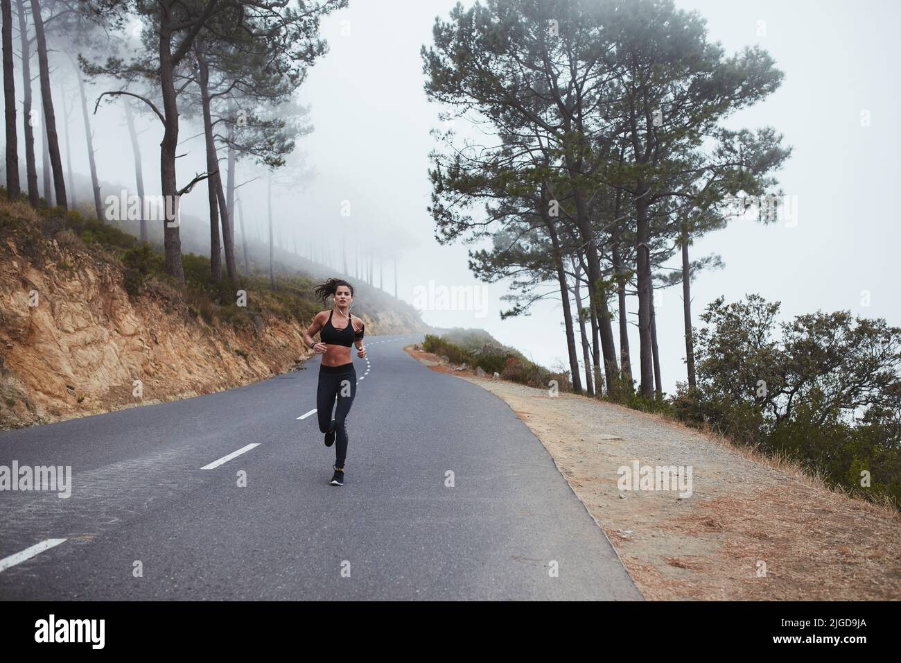 Giovane donna sportiva che corre lungo una strada di campagna al mattino. Giovane donna atletica che ha una sessione di allenamento vigorosa. Foto Stock
