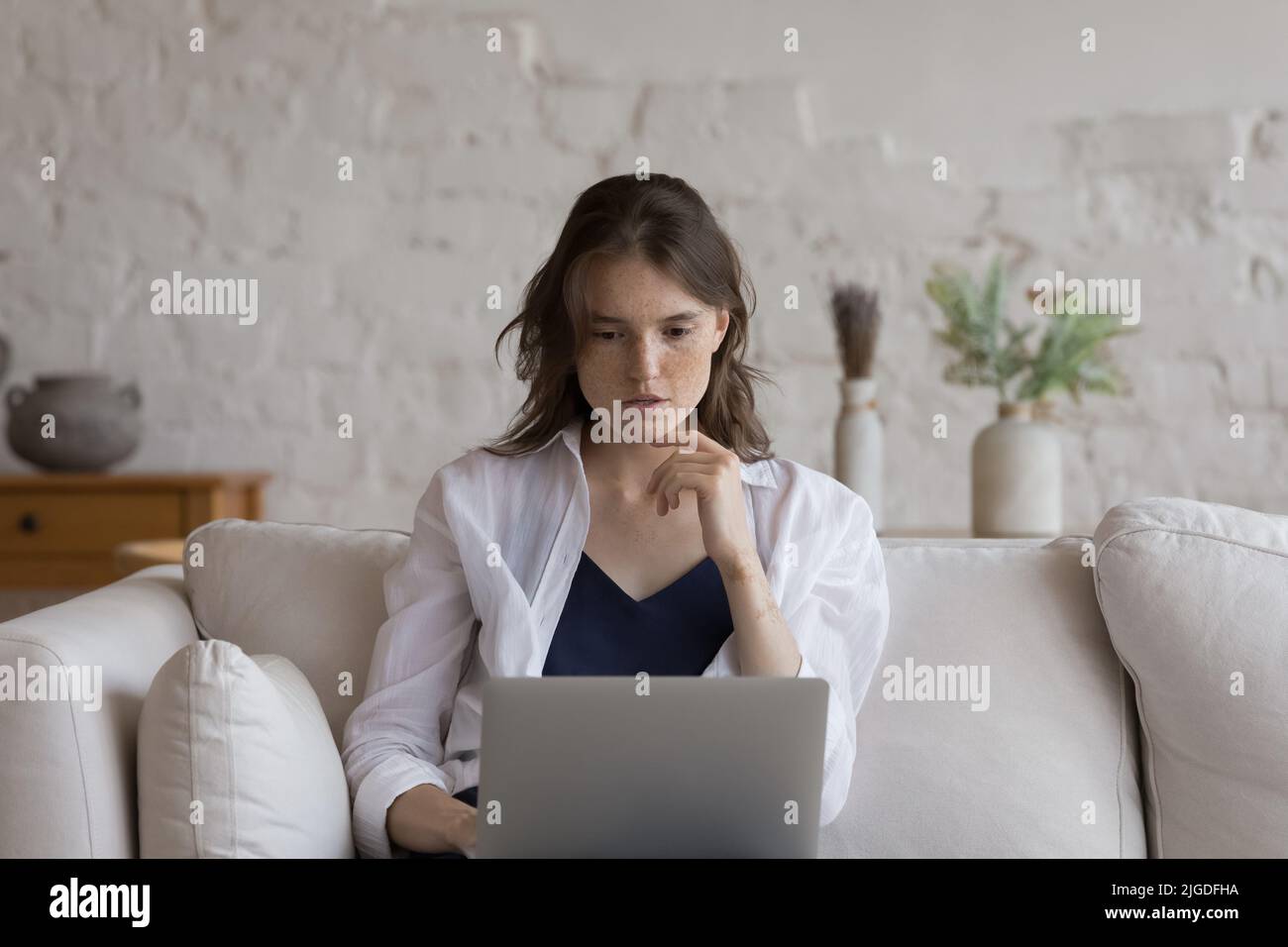 Donna giovane e pensiva che studia o lavora con un computer portatile Foto Stock