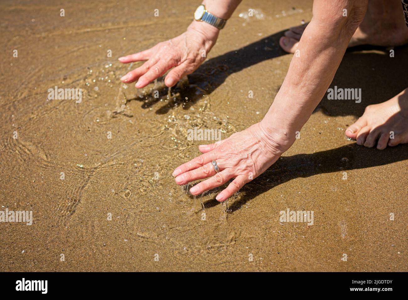 Donna anziana attraente che tocca l'acqua sulla riva del mare Foto Stock