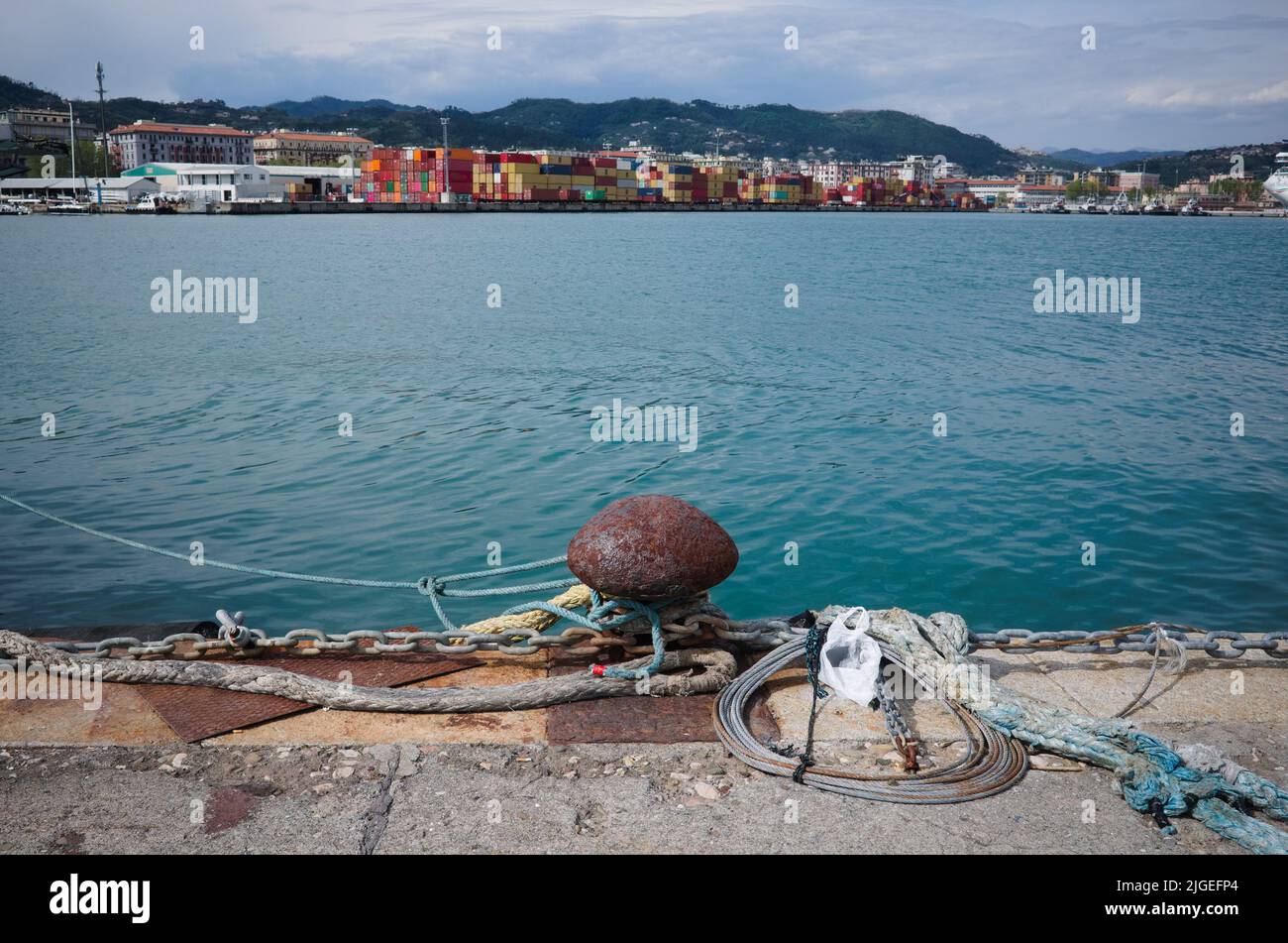 Arrugginito ormeggio con funi e catena sul molo nel porto di la Spezia, Italia. Banchina di carico con container sullo sfondo Foto Stock