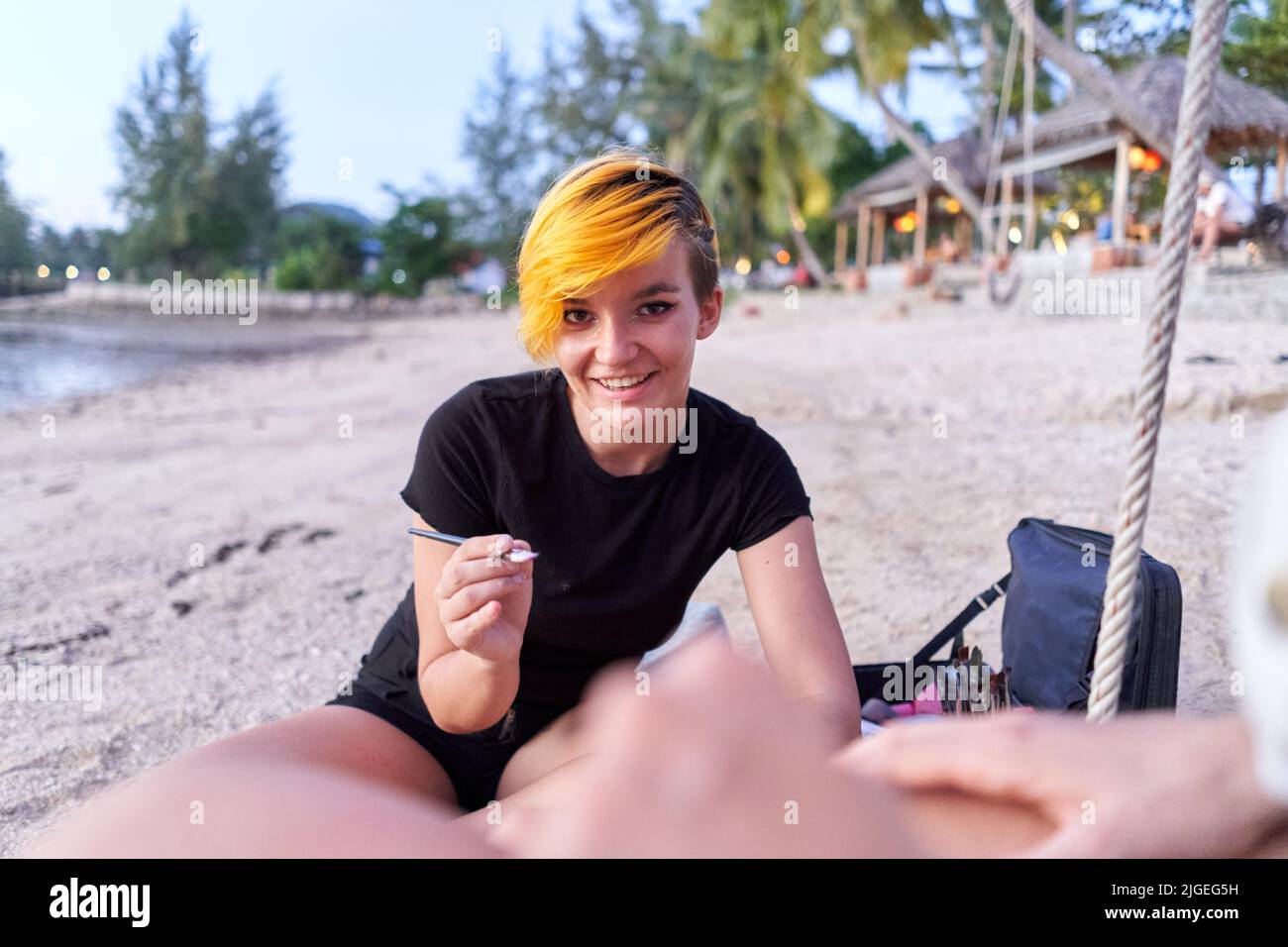 Artista che sorride alla macchina fotografica durante una sessione di body art sulla spiaggia Foto Stock