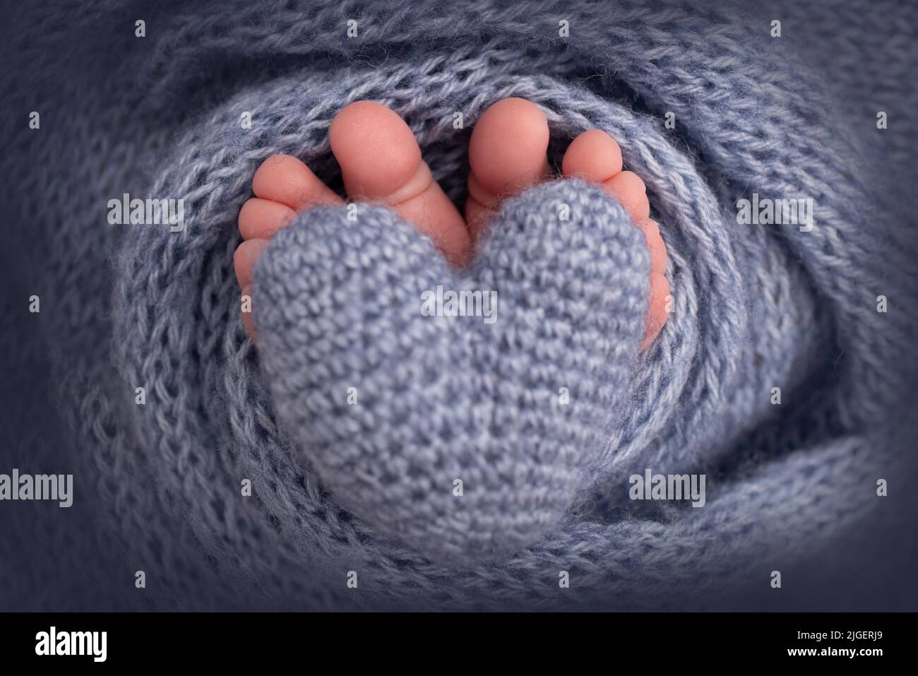 Cuore a maglia blu scuro nelle gambe di un bambino. Piedi morbidi di un nuovo nato in una coperta di lana blu scuro. Piede ravvicinato. Foto Stock