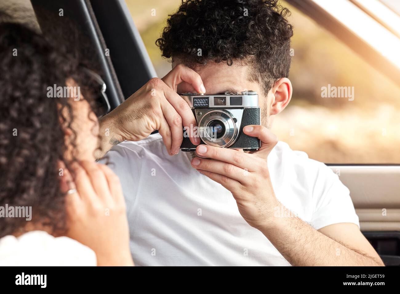 I ricordi più belli sono quelli fatti durante i viaggi su strada. Un giovane che scatta una foto della sua ragazza mentre si siede in macchina insieme. Foto Stock