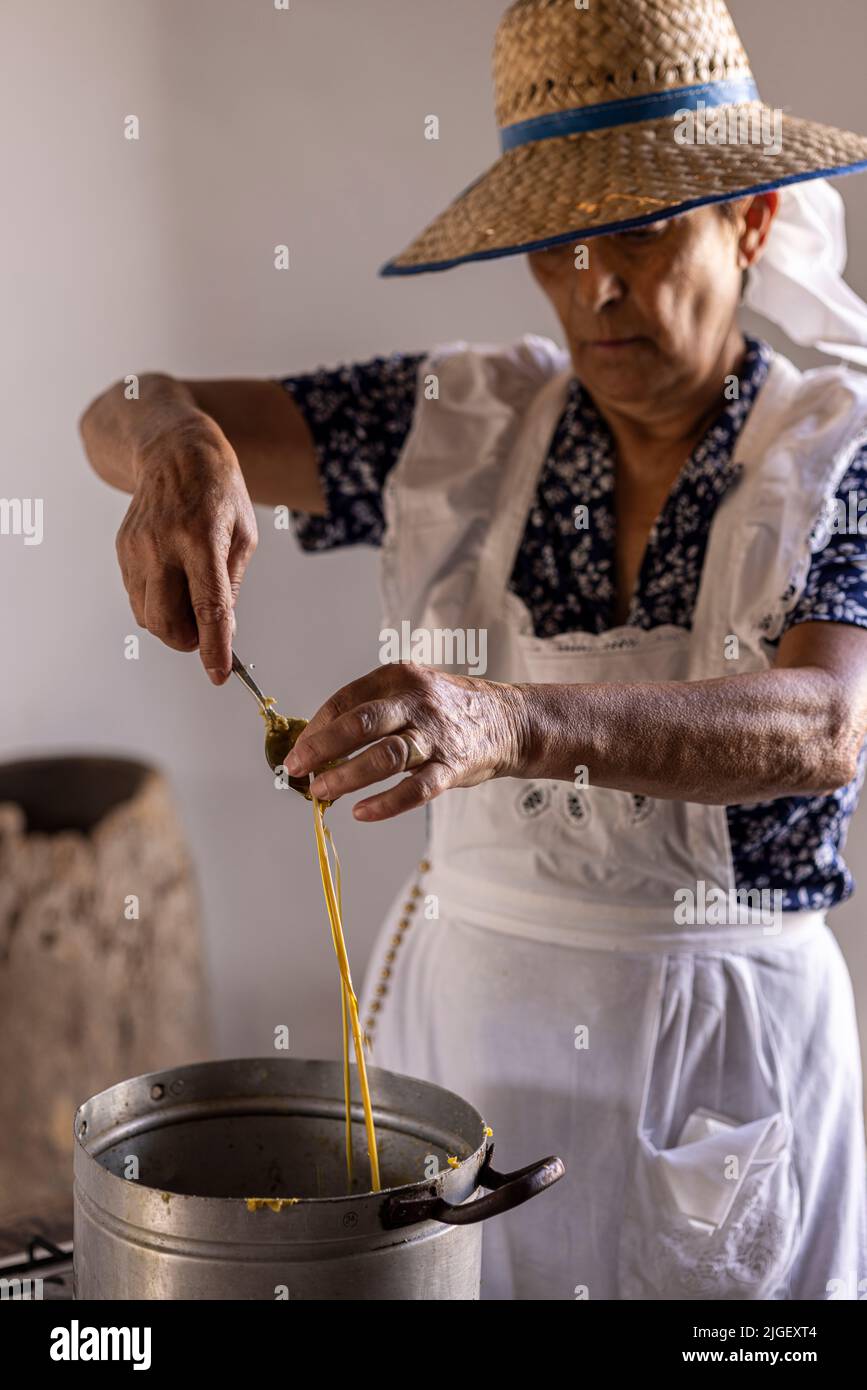 Chirche, Tenerife, 10 luglio 2022. Una donna che fa candele da cera d'api versando la cera fusa da un cucchiaio sopra una corda. Gli abitanti del villaggio celebrano il Día de tradiciones, giorno delle Tradizioni nel piccolo villaggio di montagna dove si rievadono le scene dello stile di vita rurale vissuto dai loro antenati nel 1940s Foto Stock
